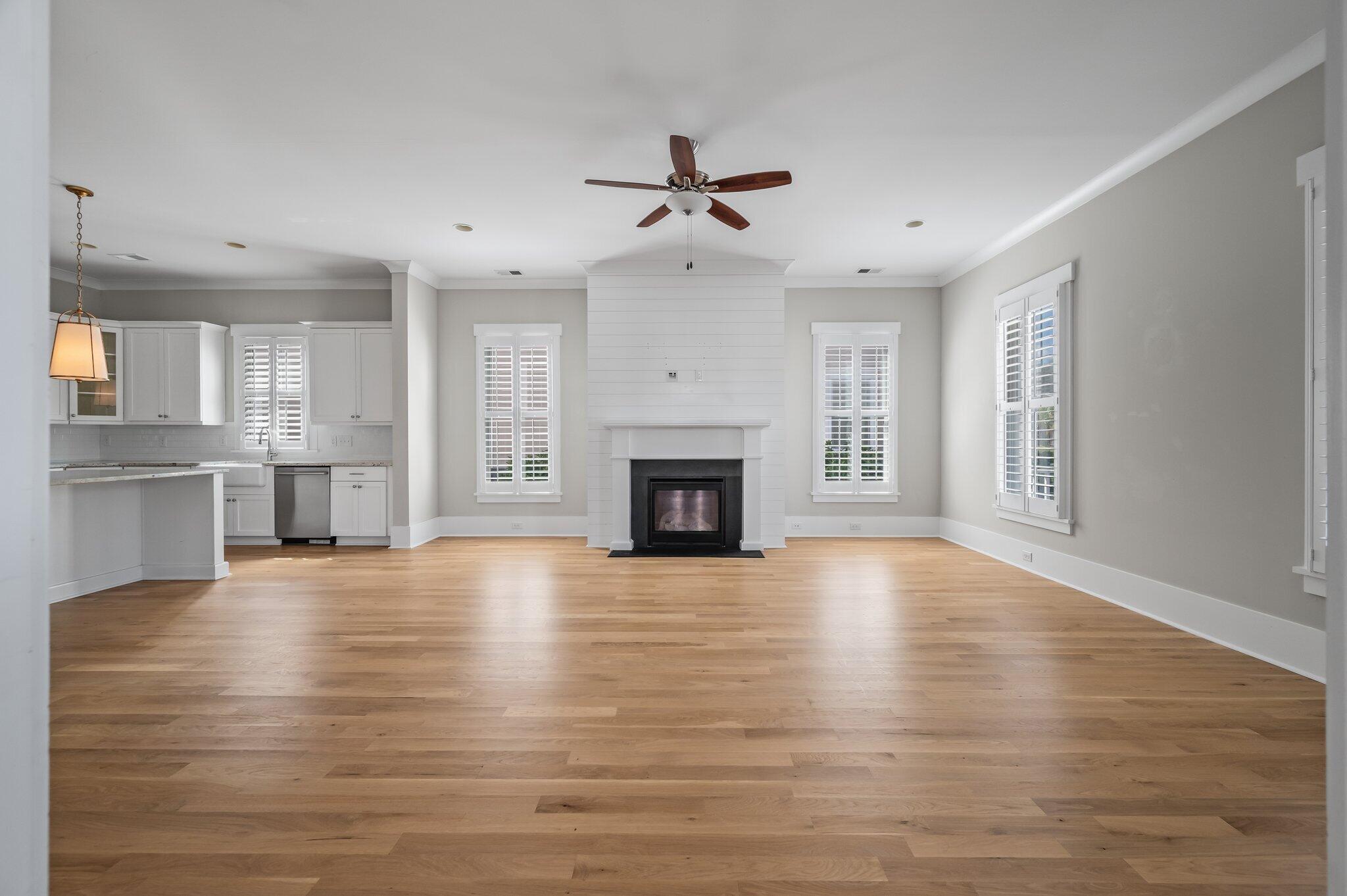 Open living room and kitchen with a white fireplace, plantation shutters, and hardwood floors.