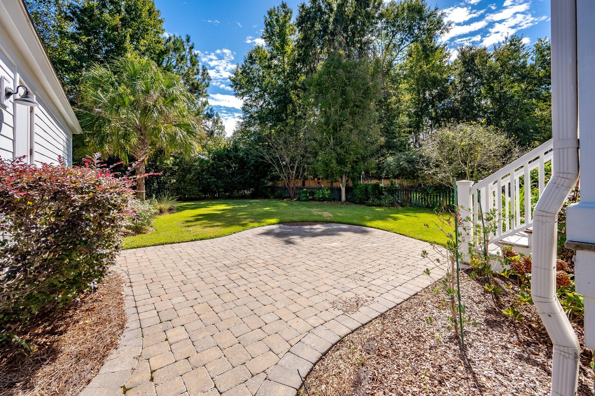Backyard patio with a curved paver terrace, lawn, and mature trees.