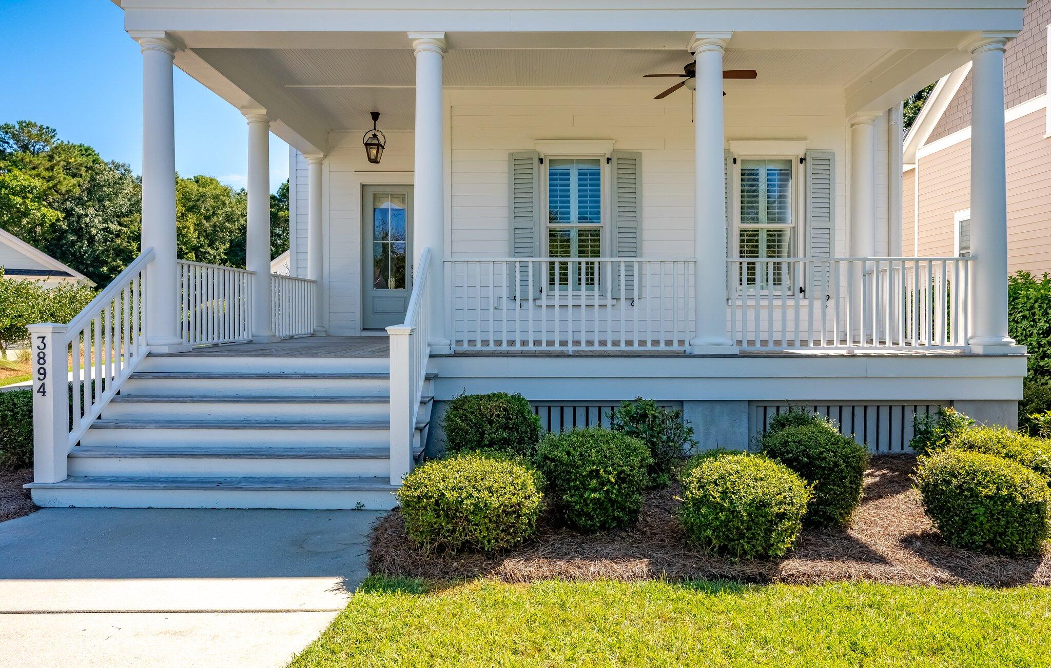 White house front porch with broad steps, columned roof, gray shutters, and clipped shrubs.