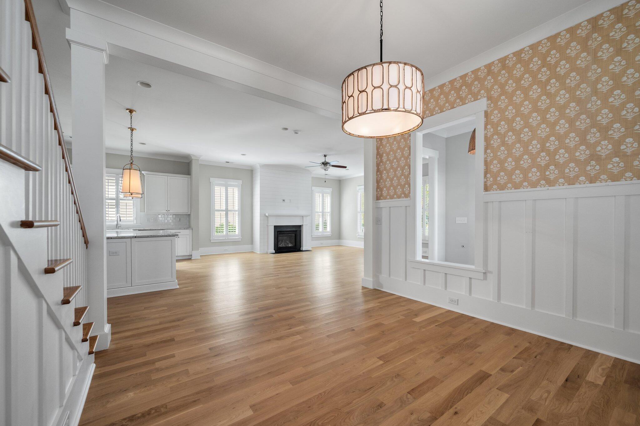 Open living room with hardwood floors, fireplace, and adjoining white kitchen.