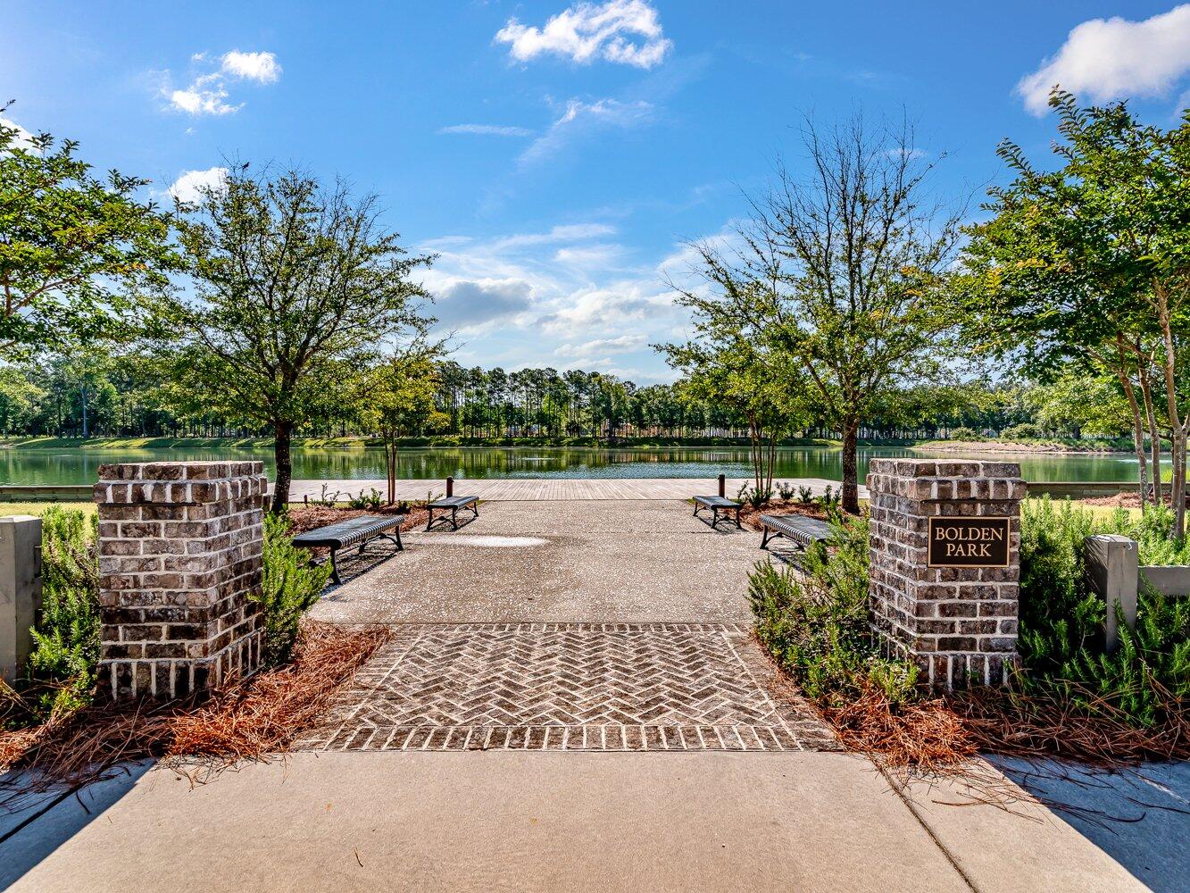 Bolden Park lakeside walkway with benches and brick entrance pillars.