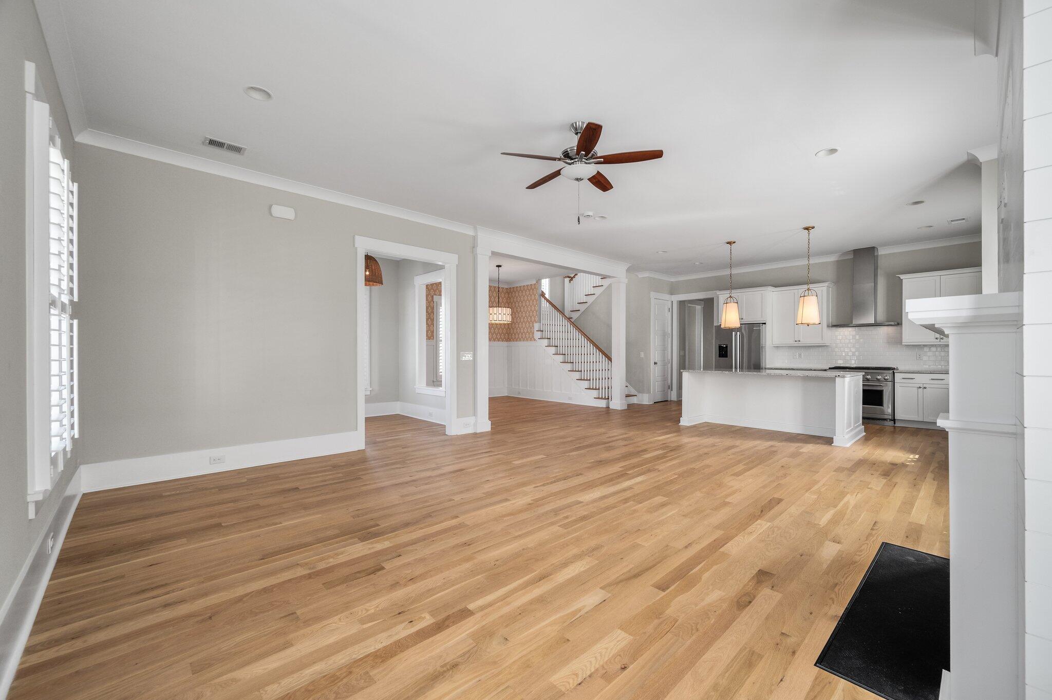 Open living area and kitchen with hardwood floors, white cabinetry, and a staircase.