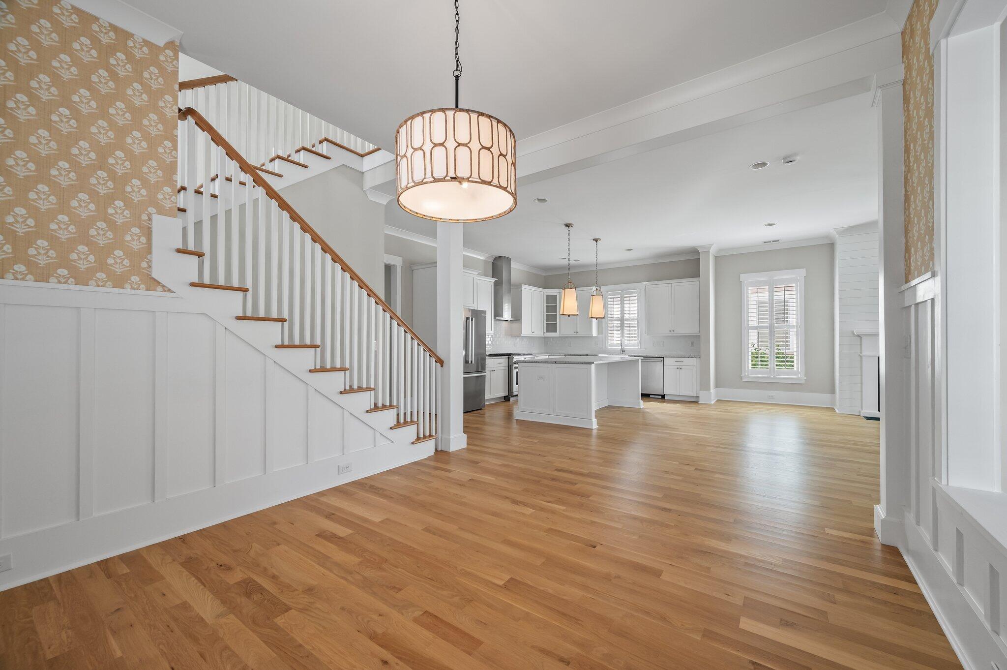 Open kitchen and living area with hardwood floors, a staircase, and white cabinetry.
