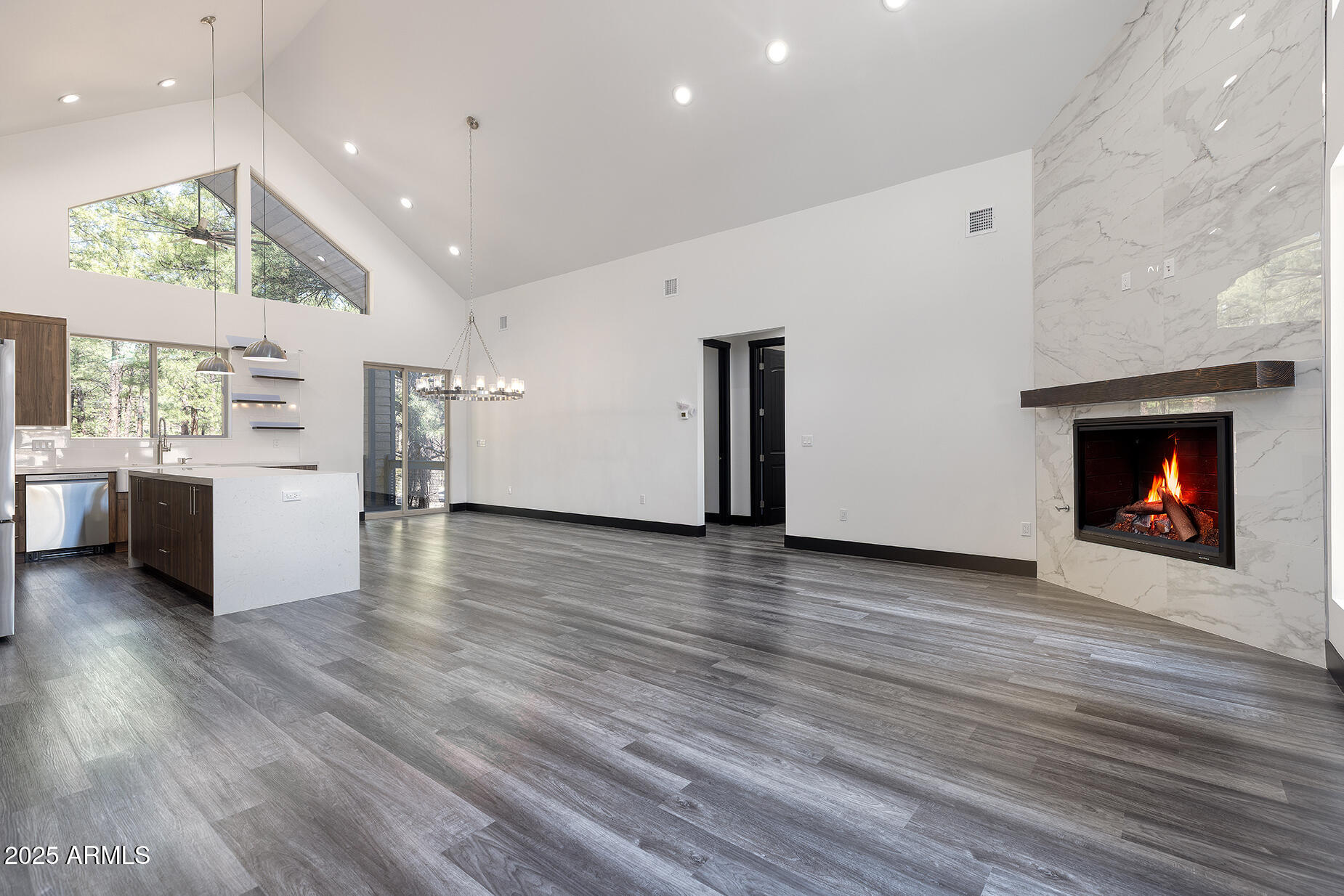 Open living room and kitchen with vaulted ceilings, a marble-look fireplace, and gray plank flooring.