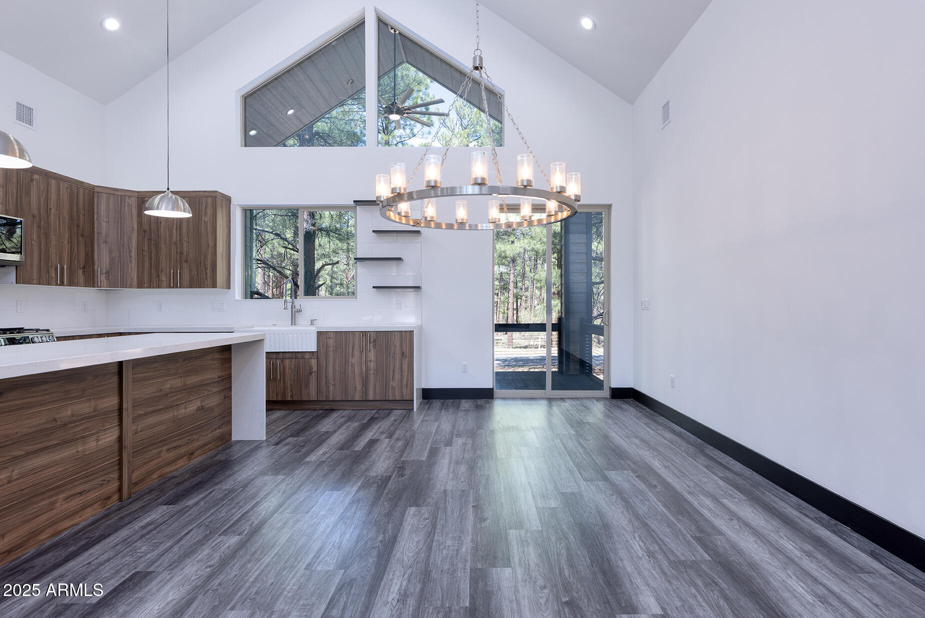 Modern kitchen with walnut-tone cabinets, a white island, and a circular chandelier beneath tall windows.