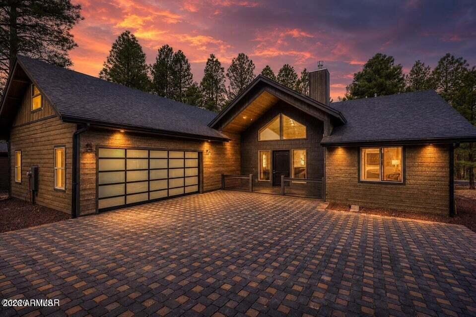 Wood-sided home with a broad paver driveway and garage beneath a colorful sunset sky.