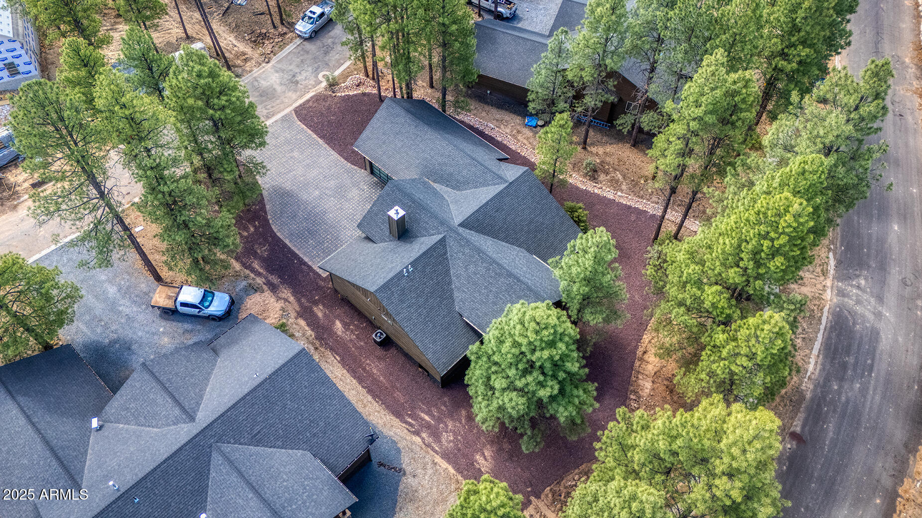 Aerial view of a gray-roofed home and paved driveway among pine trees.