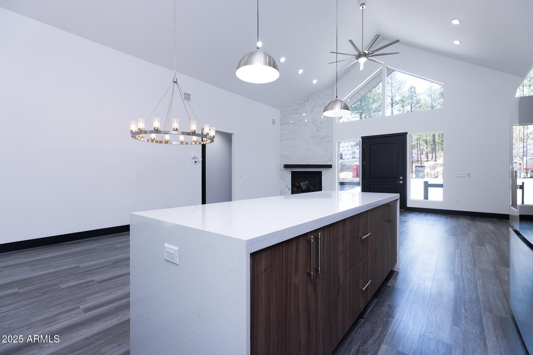 Open-plan kitchen with a large white waterfall island, vaulted ceiling, and marble-look fireplace.