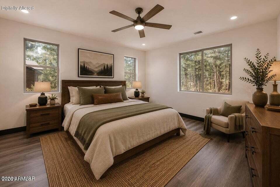 Staged bedroom with a large bed, dark wood furnishings, and windows overlooking pine trees.