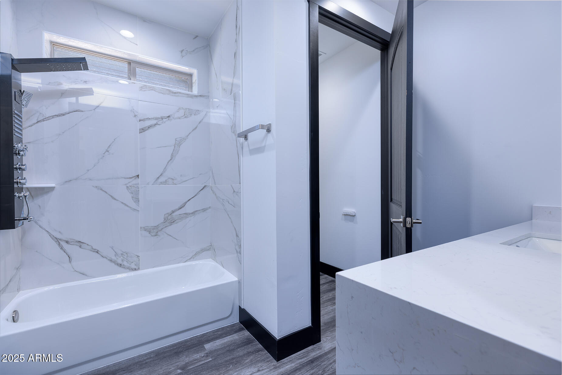 Modern bathroom with a marble-look tiled tub and shower and a broad white vanity counter.