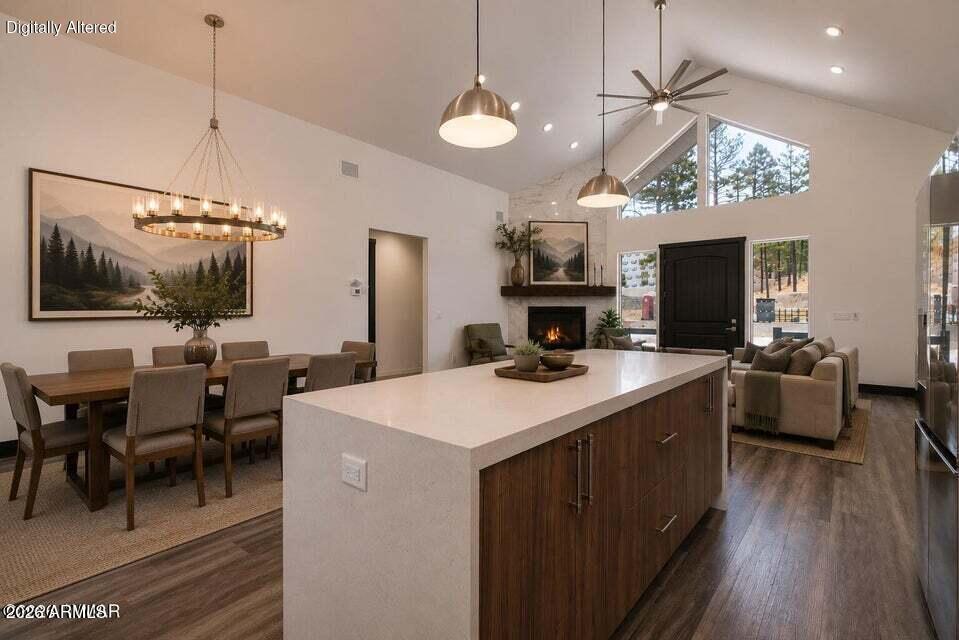 Open-plan kitchen with a large white island, dining area, fireplace, and vaulted ceiling.