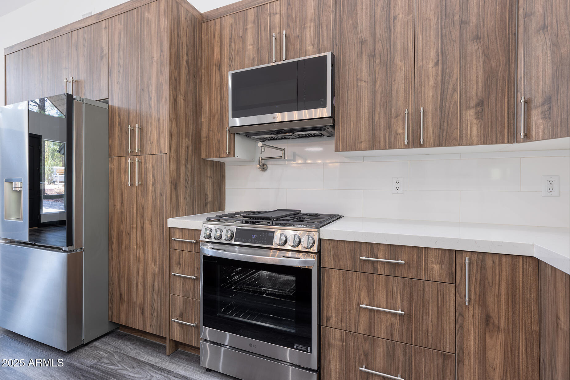 Kitchen with walnut-toned cabinetry, white backsplash, stainless refrigerator, and gas range.