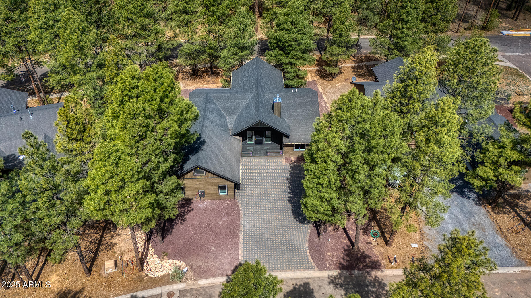 Aerial view of a pine-surrounded home with a broad paved driveway.