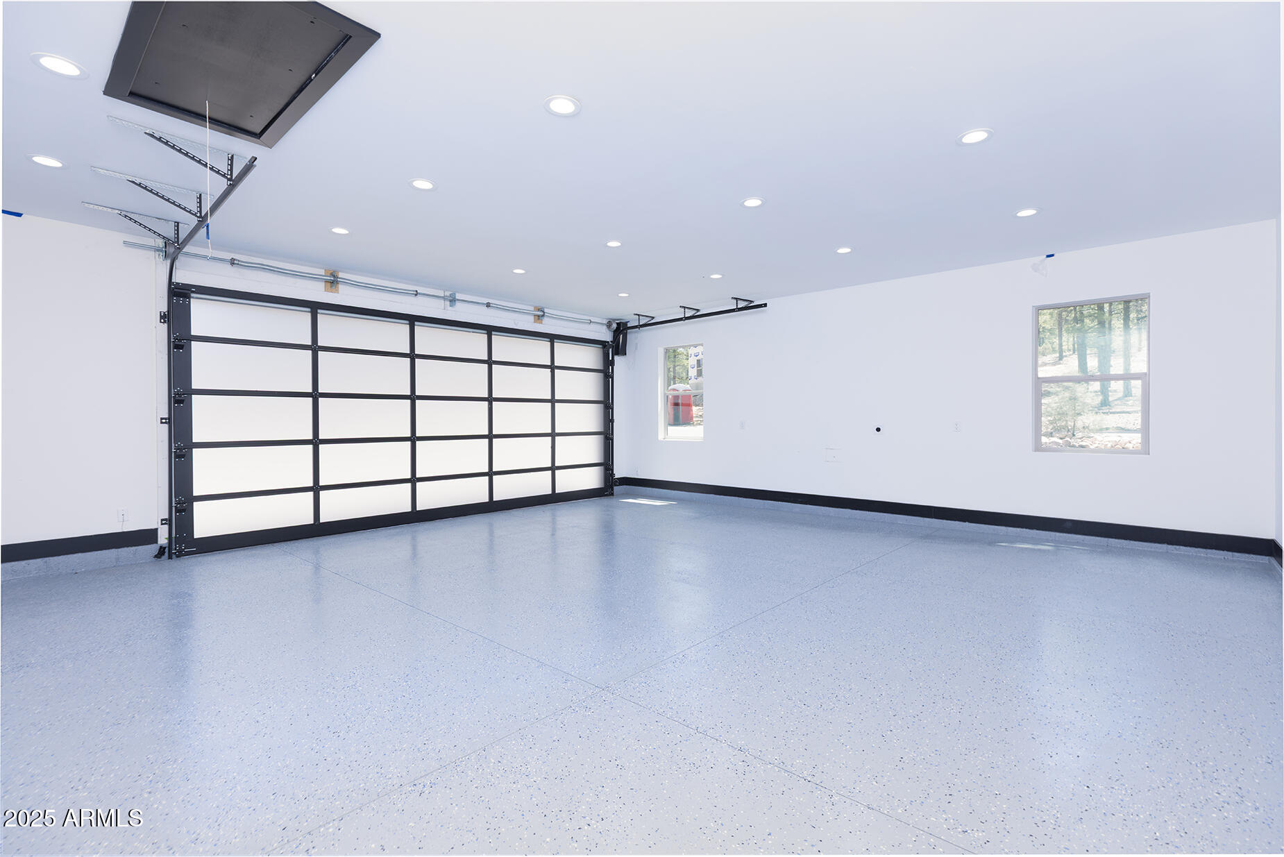 Empty garage with a speckled epoxy floor, black-framed door, recessed lights, and two windows.