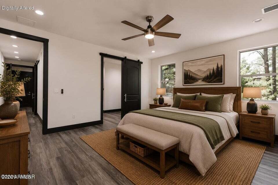 Staged bedroom with olive-green and white bedding, dark wood furniture, and windows overlooking trees.