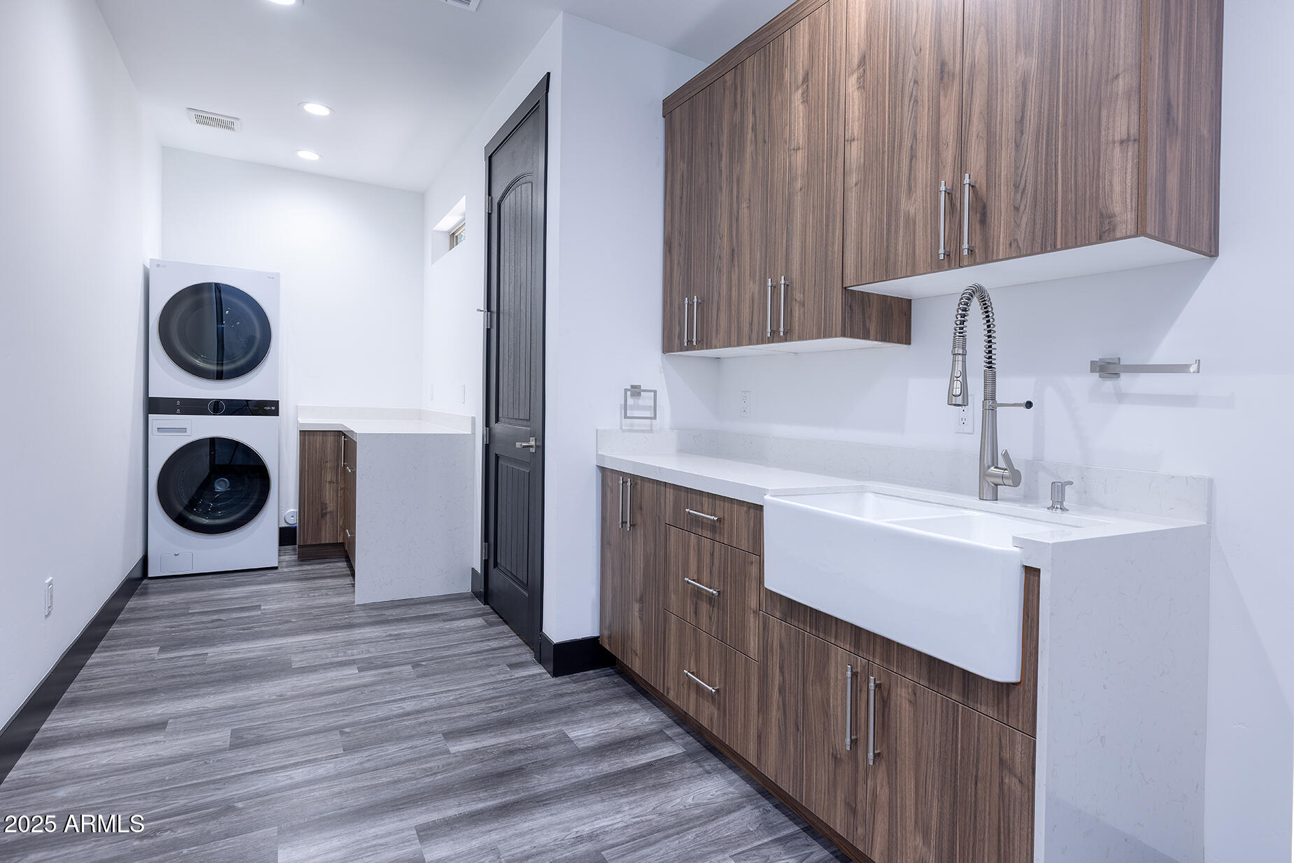 Laundry room with stacked washer and dryer, walnut cabinets, and a large farmhouse sink.