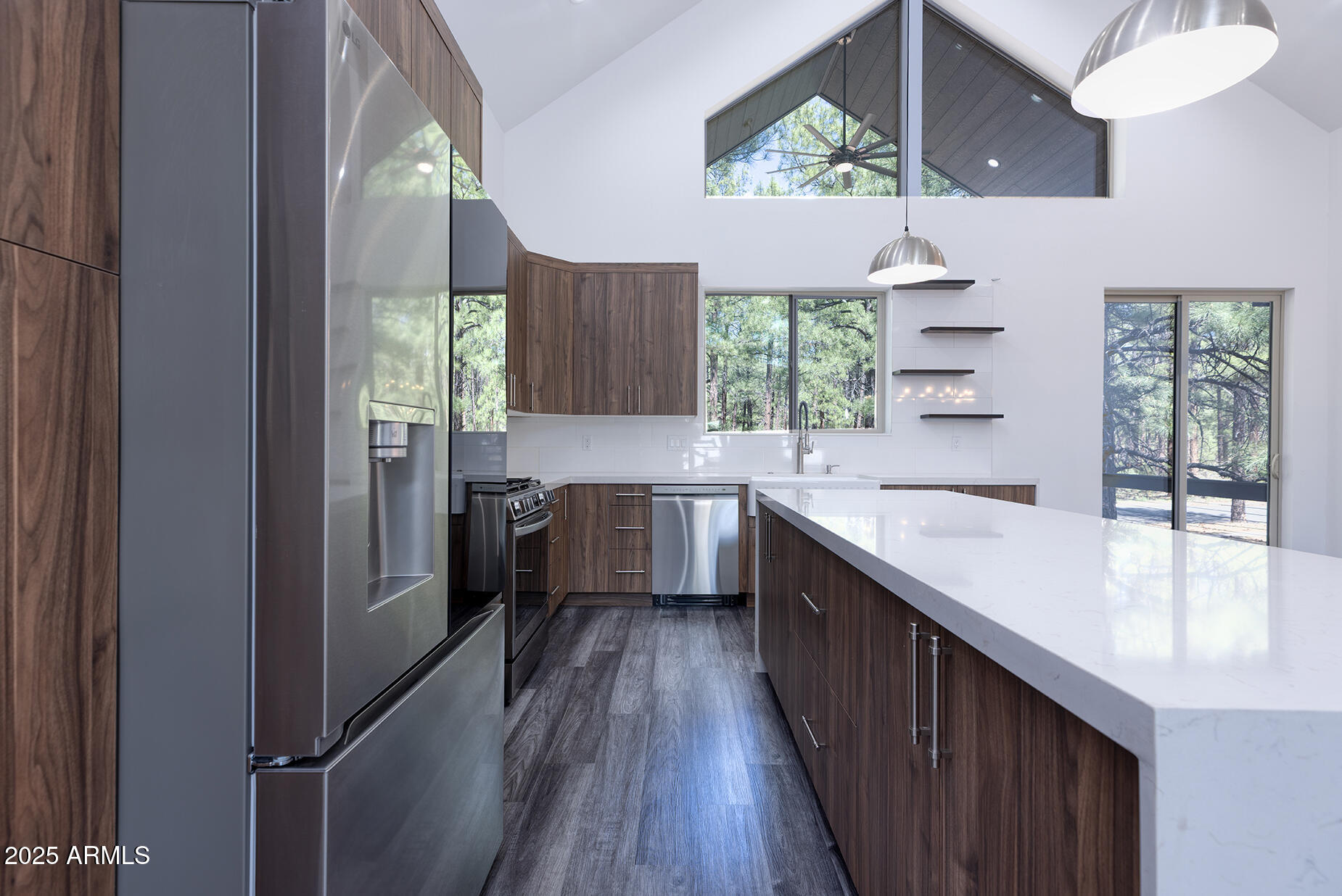 Modern kitchen with dark wood cabinets, stainless steel appliances, and a large white island beneath vaulted ceilings.