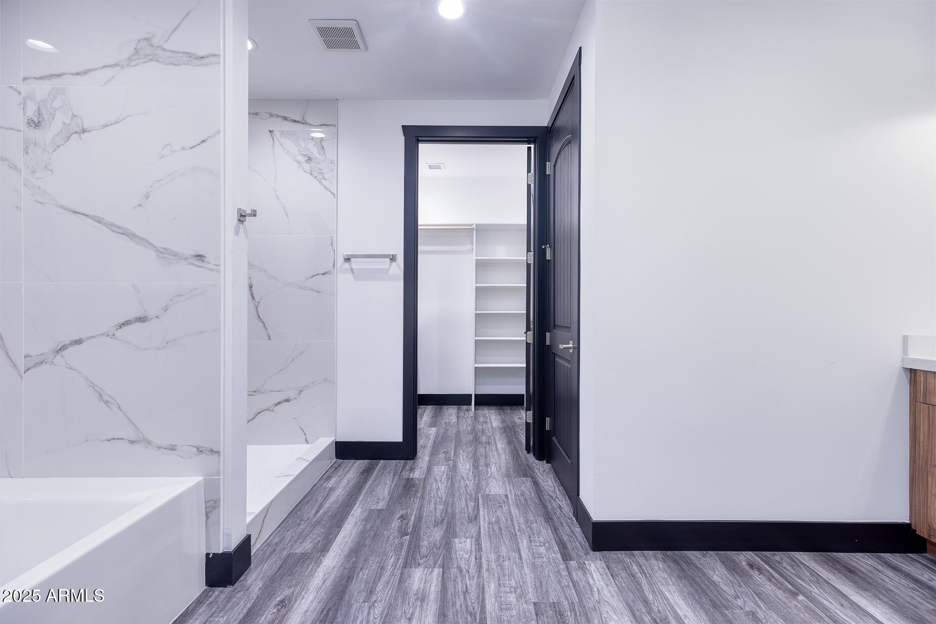 Bathroom with marble-look tile, a white tub, and an open doorway to a shelved walk-in closet.