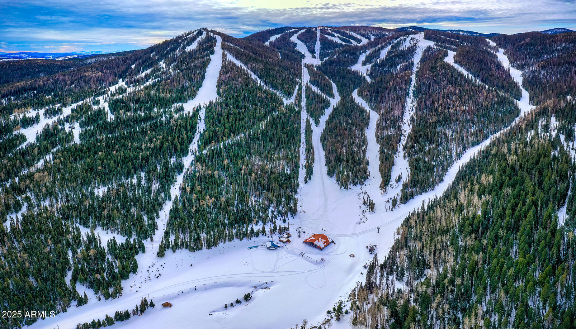 Aerial view of a ski resort with snowy runs winding through evergreen forest.
