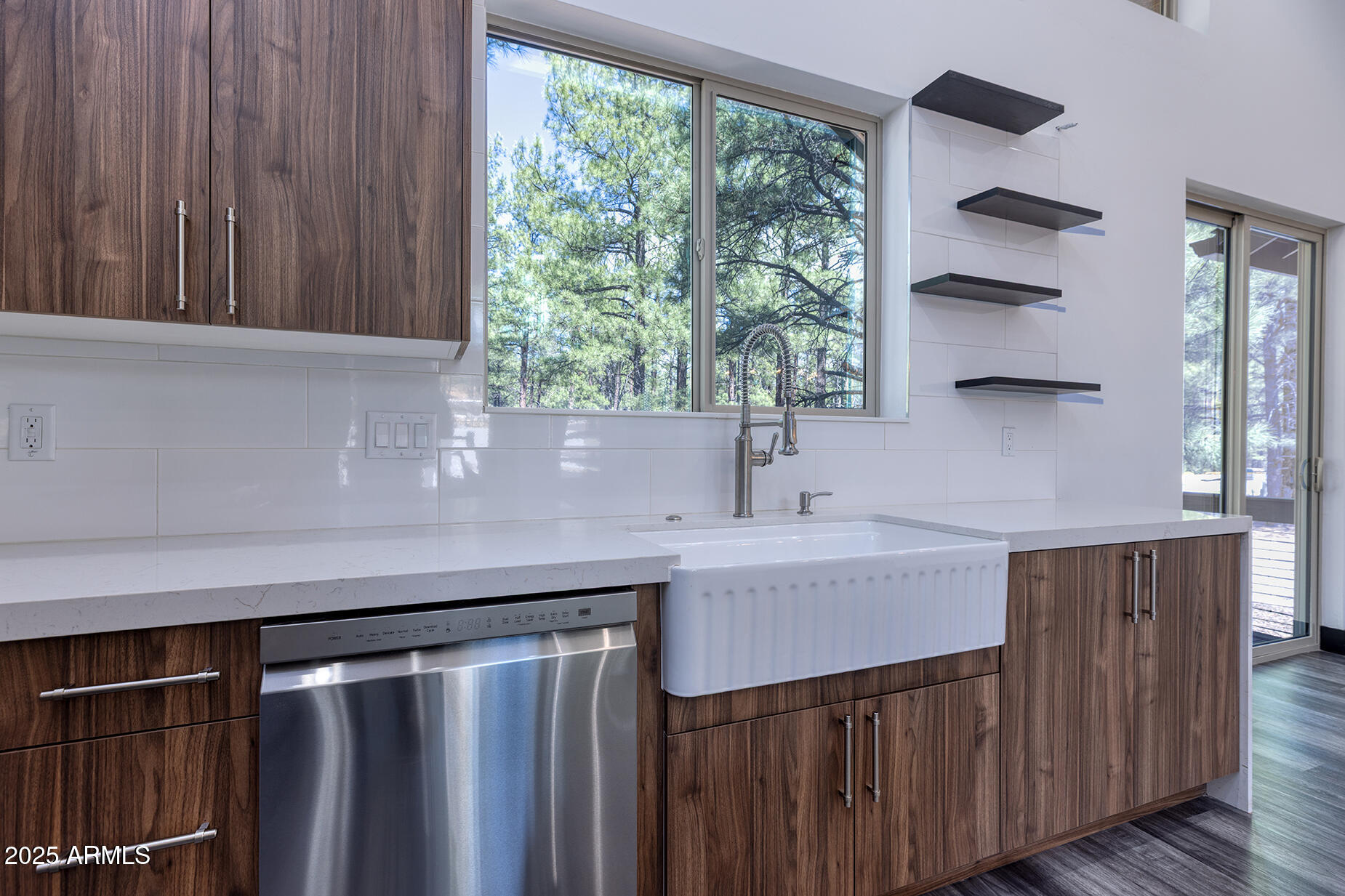 Modern kitchen with dark wood cabinets, a farmhouse sink, and windows overlooking pine trees.