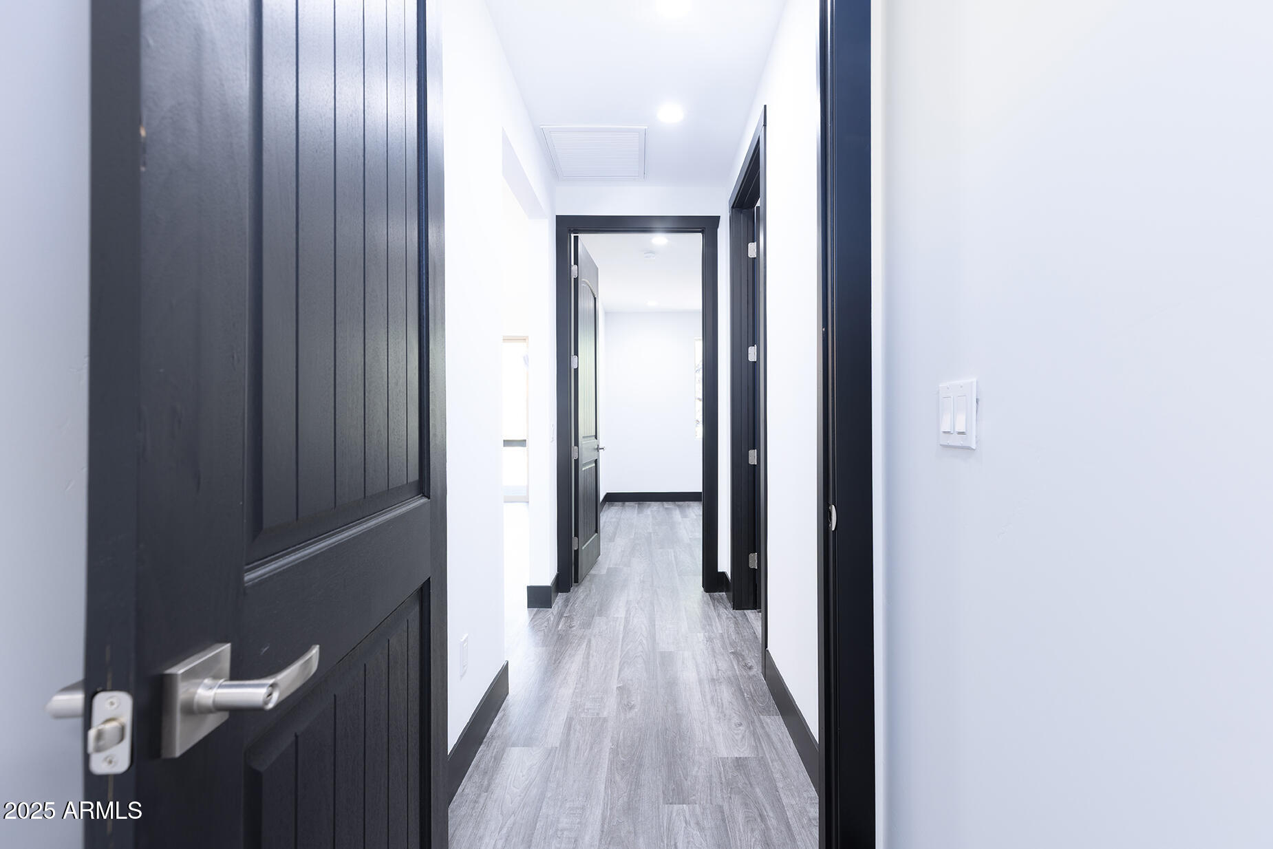 Interior hallway with gray plank flooring and black doors and trim.
