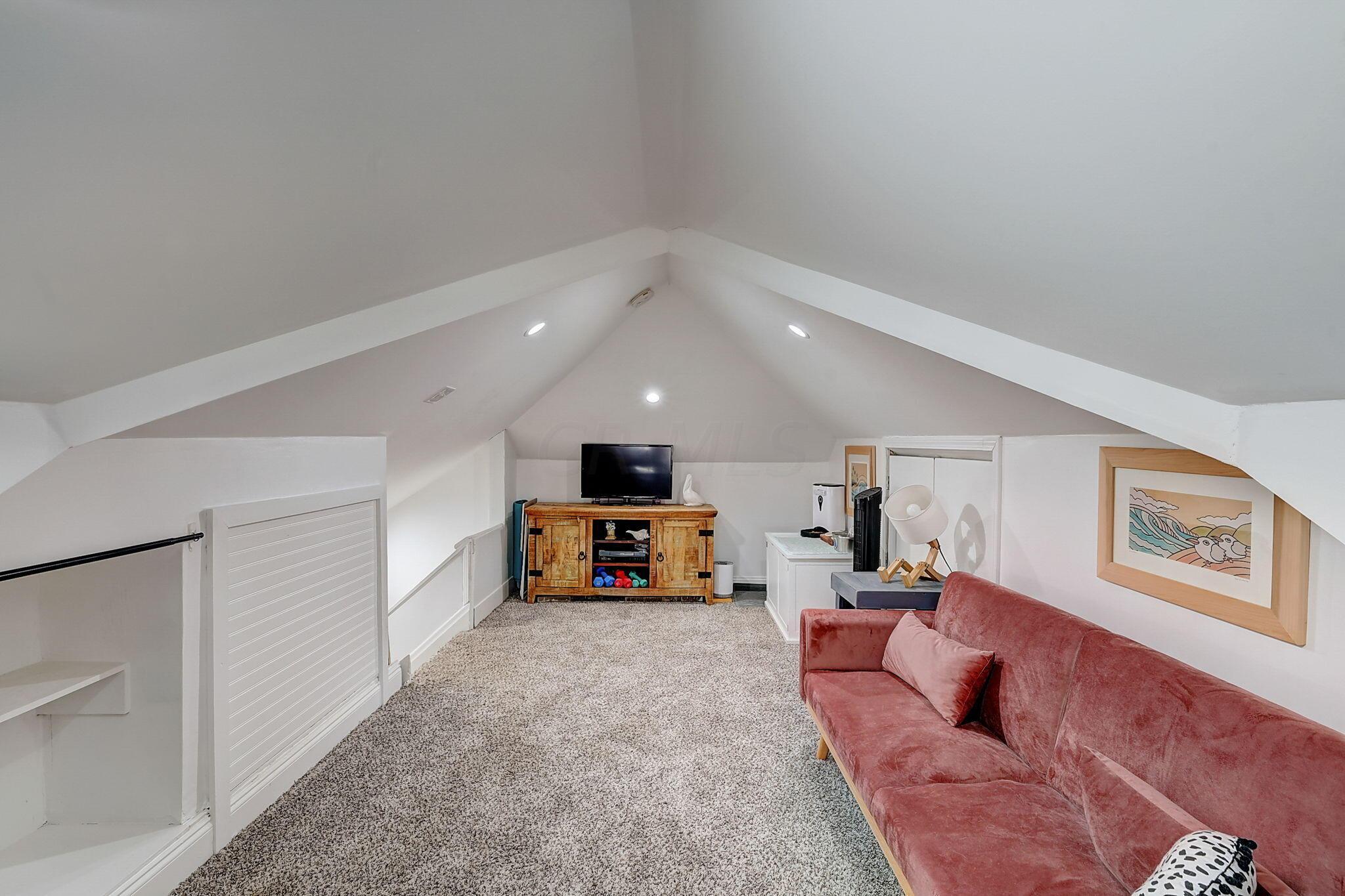 Attic living area with a vaulted ceiling, red sofa, carpet, and television.
