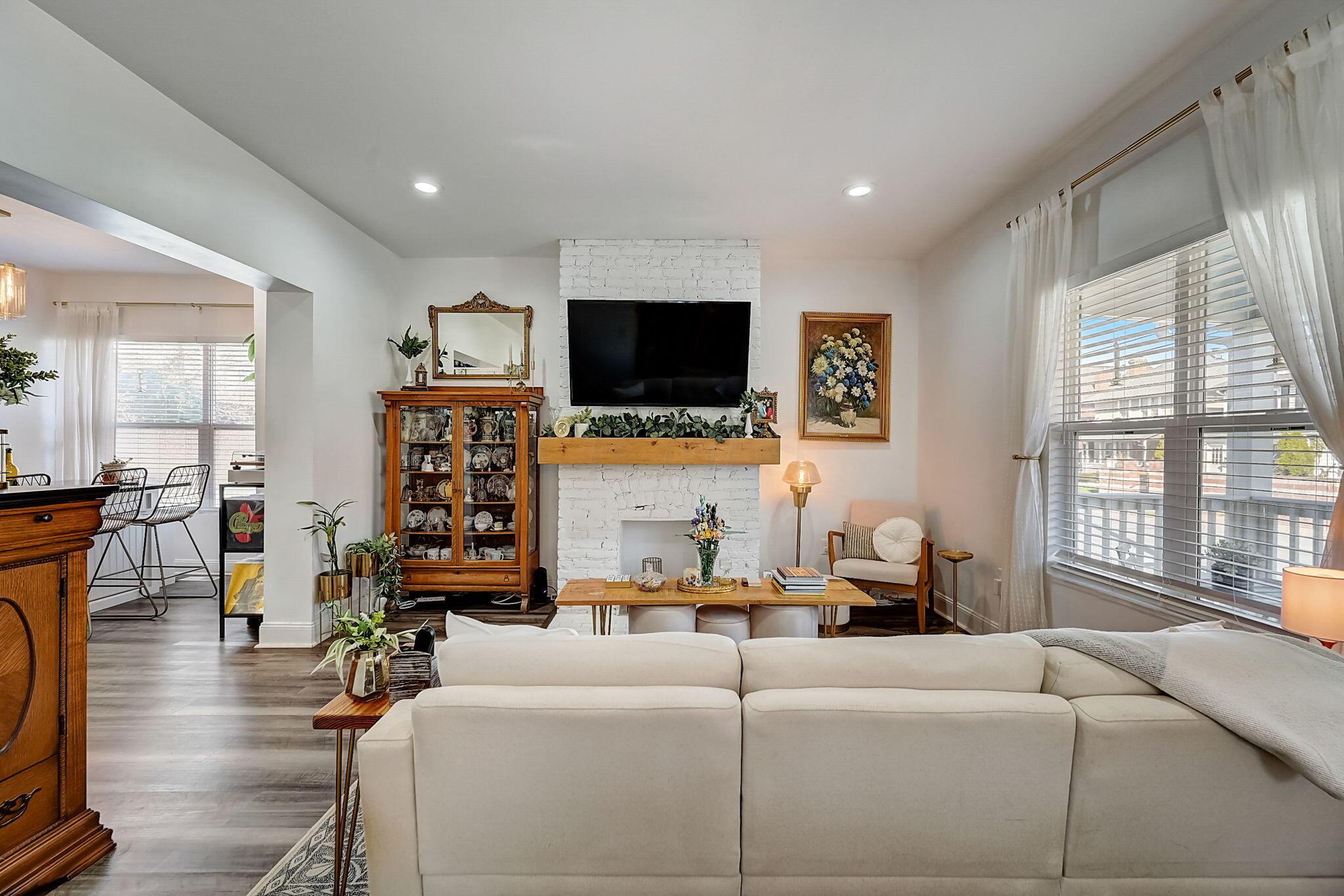 Living room with a white brick fireplace, mounted television, and large curtained windows.