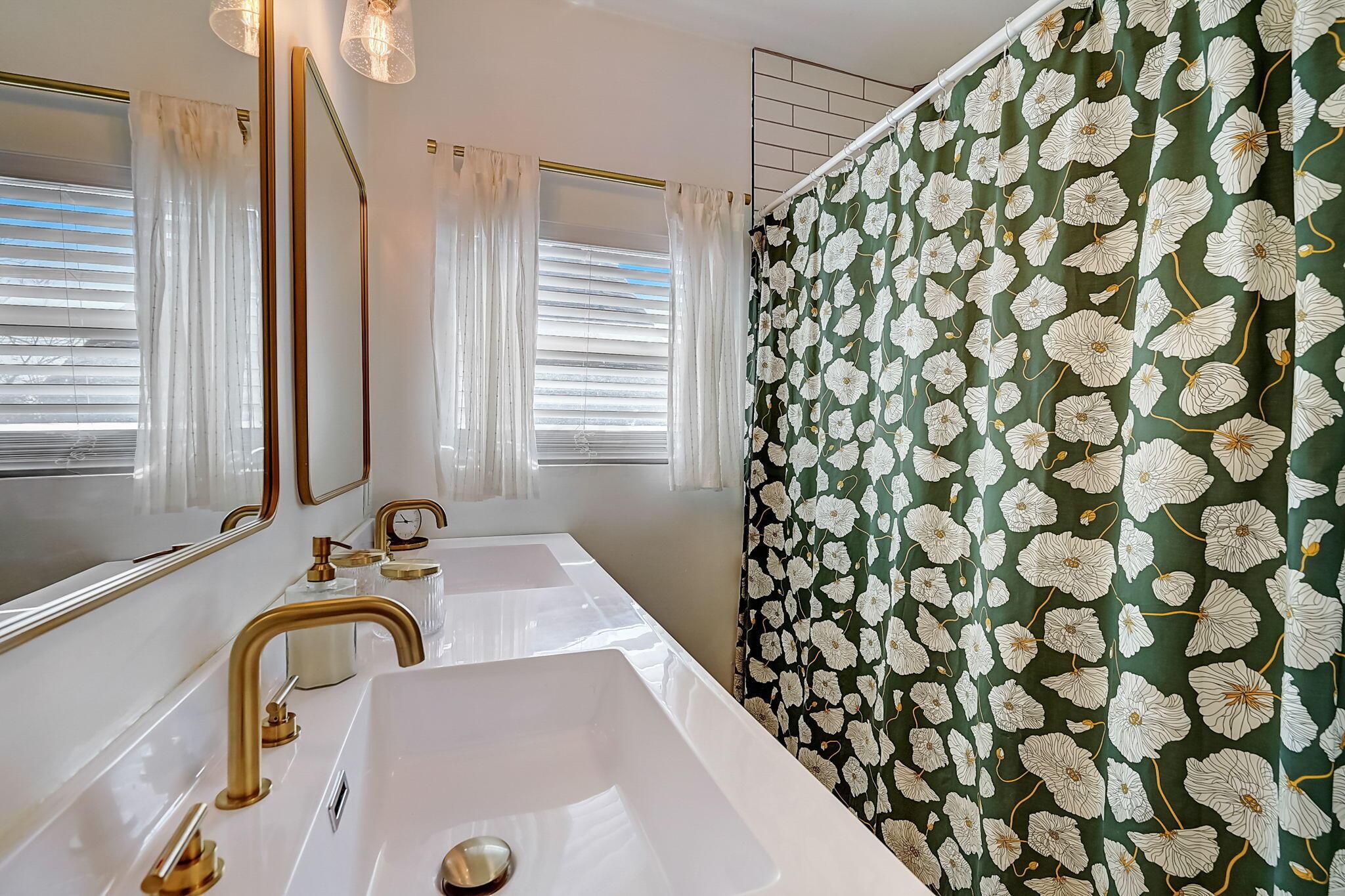 Bathroom with a white double vanity, brass faucets, and a green floral shower curtain.