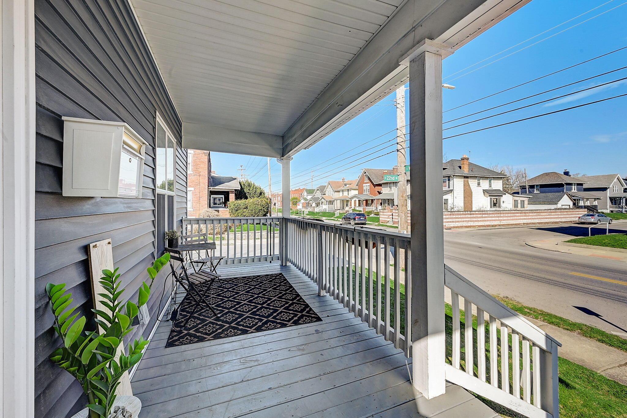 Covered gray front porch with white railings, a patterned rug, and seating overlooking a residential street.