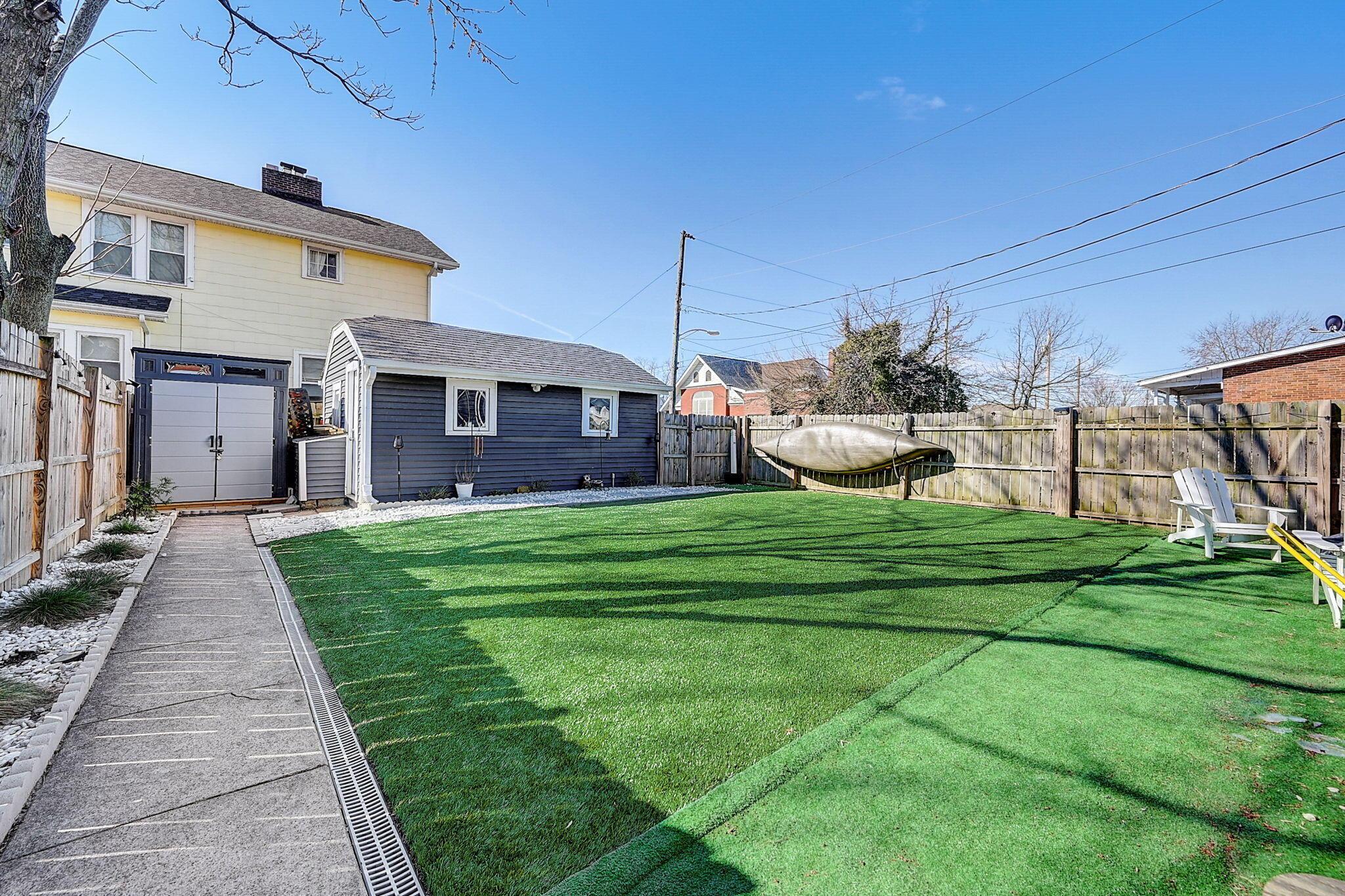 Fenced backyard with artificial turf, a detached shed, and a concrete walkway.