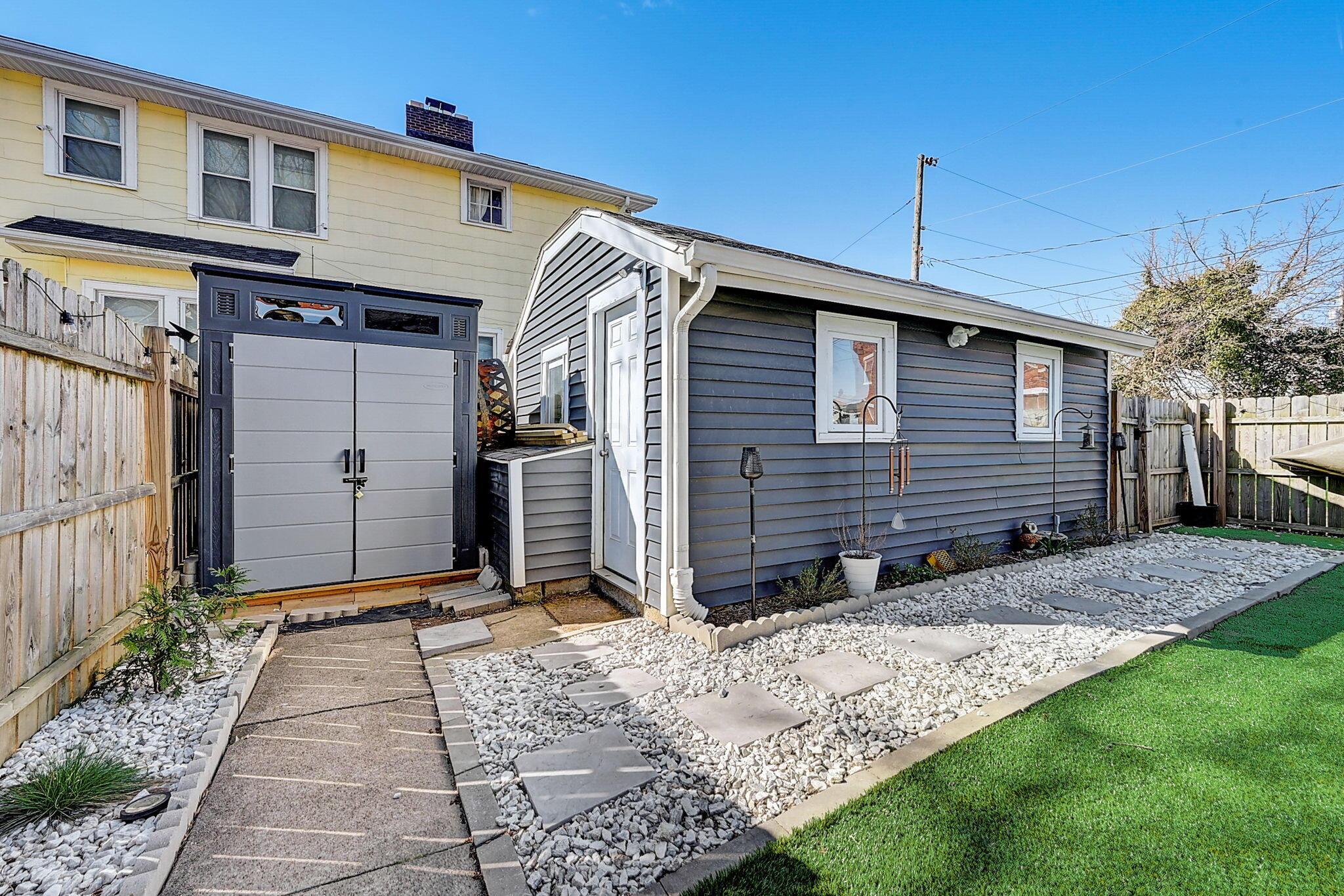 Blue-gray detached garage beside a house, with a stepping-stone path through white stone landscaping.