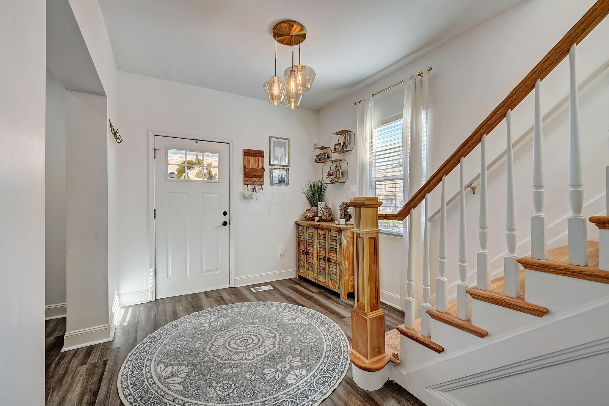 Entry foyer with a patterned rug, rustic cabinet, and staircase with a wood handrail.