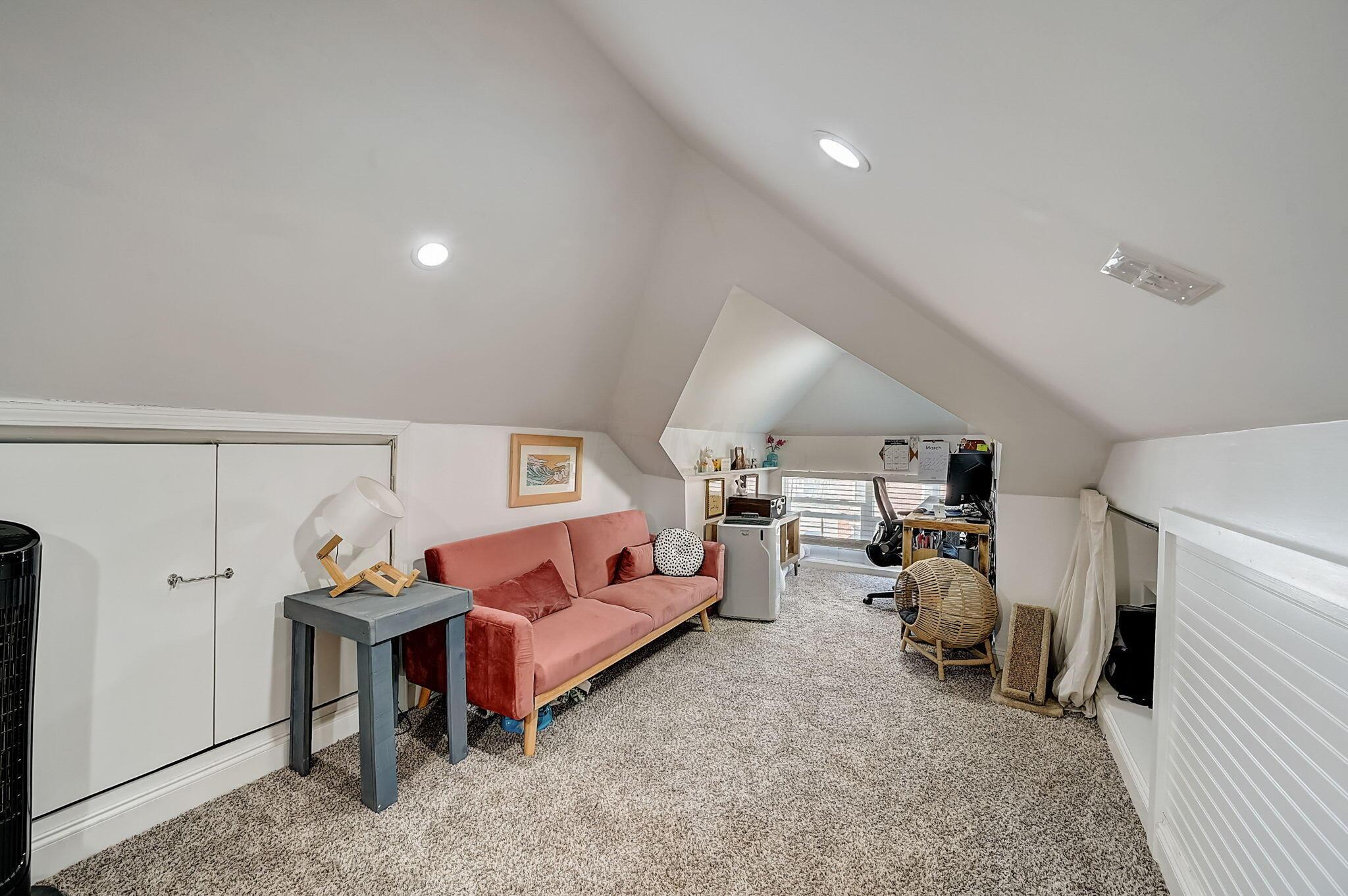 Finished attic office and lounge with a pink sofa, desk, and sloped ceiling.