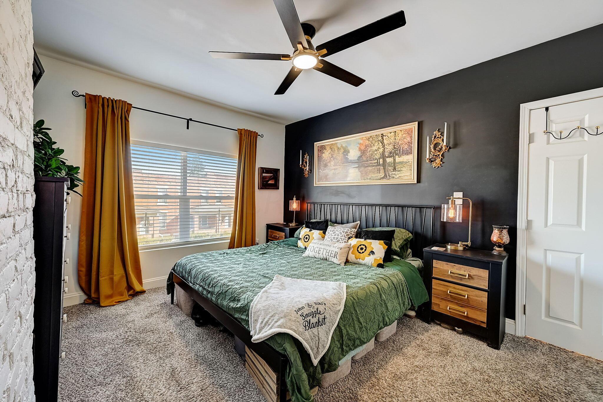 Bedroom with a green-covered bed, mustard curtains, and a dark accent wall.