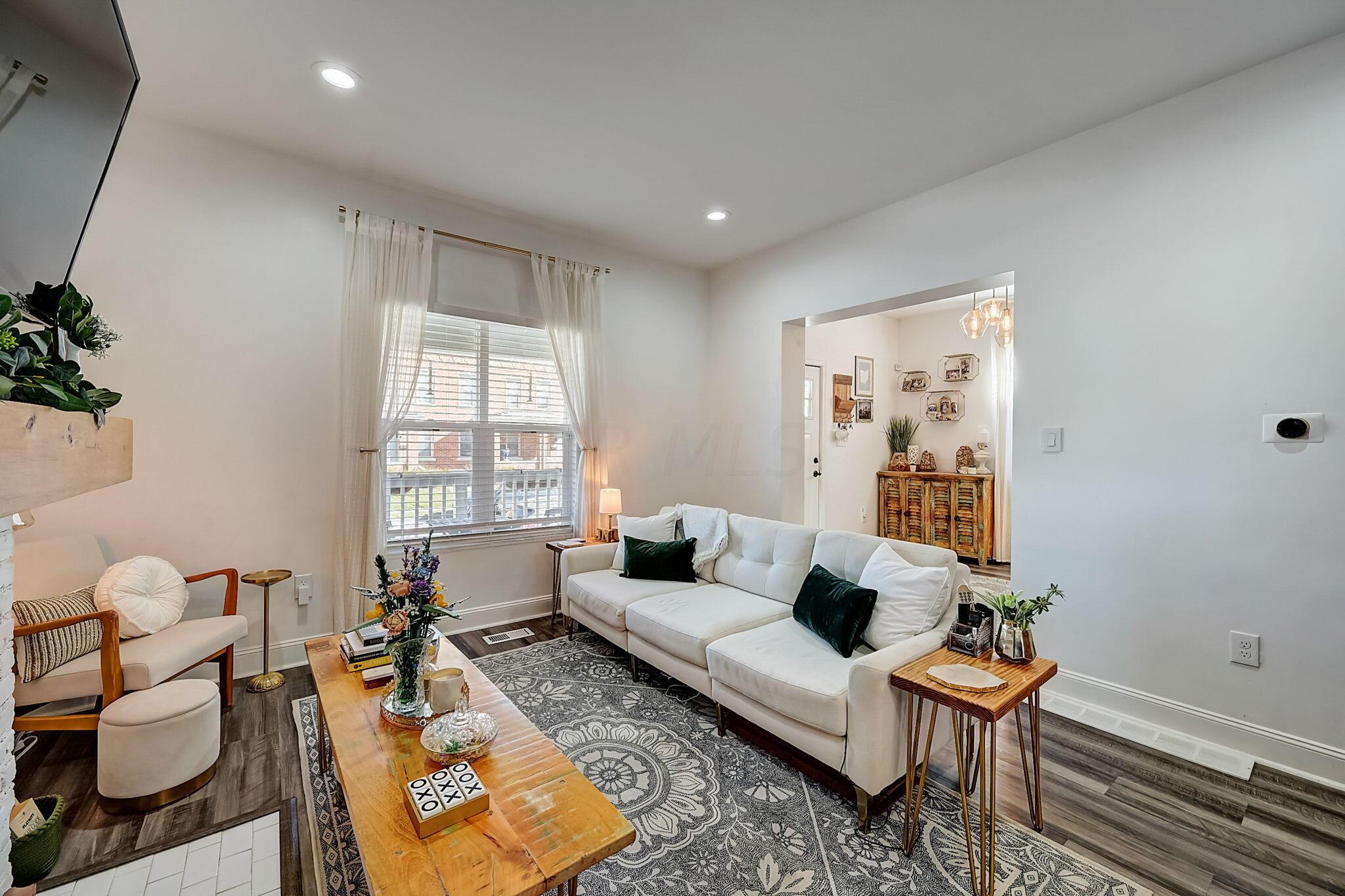 Staged living room with a white sectional, patterned rug, and large curtained window.