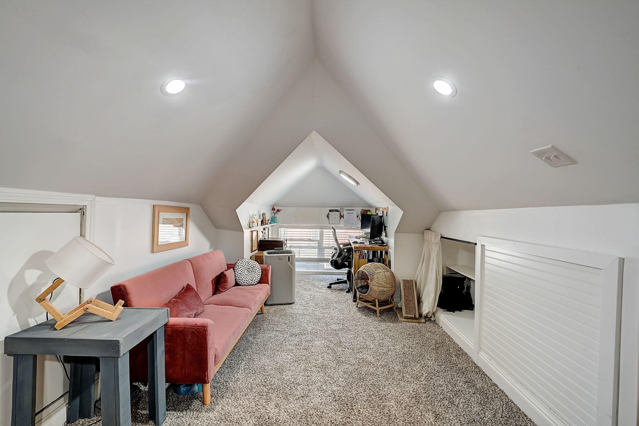 Finished attic lounge with pink sofa and a desk in the dormer alcove.