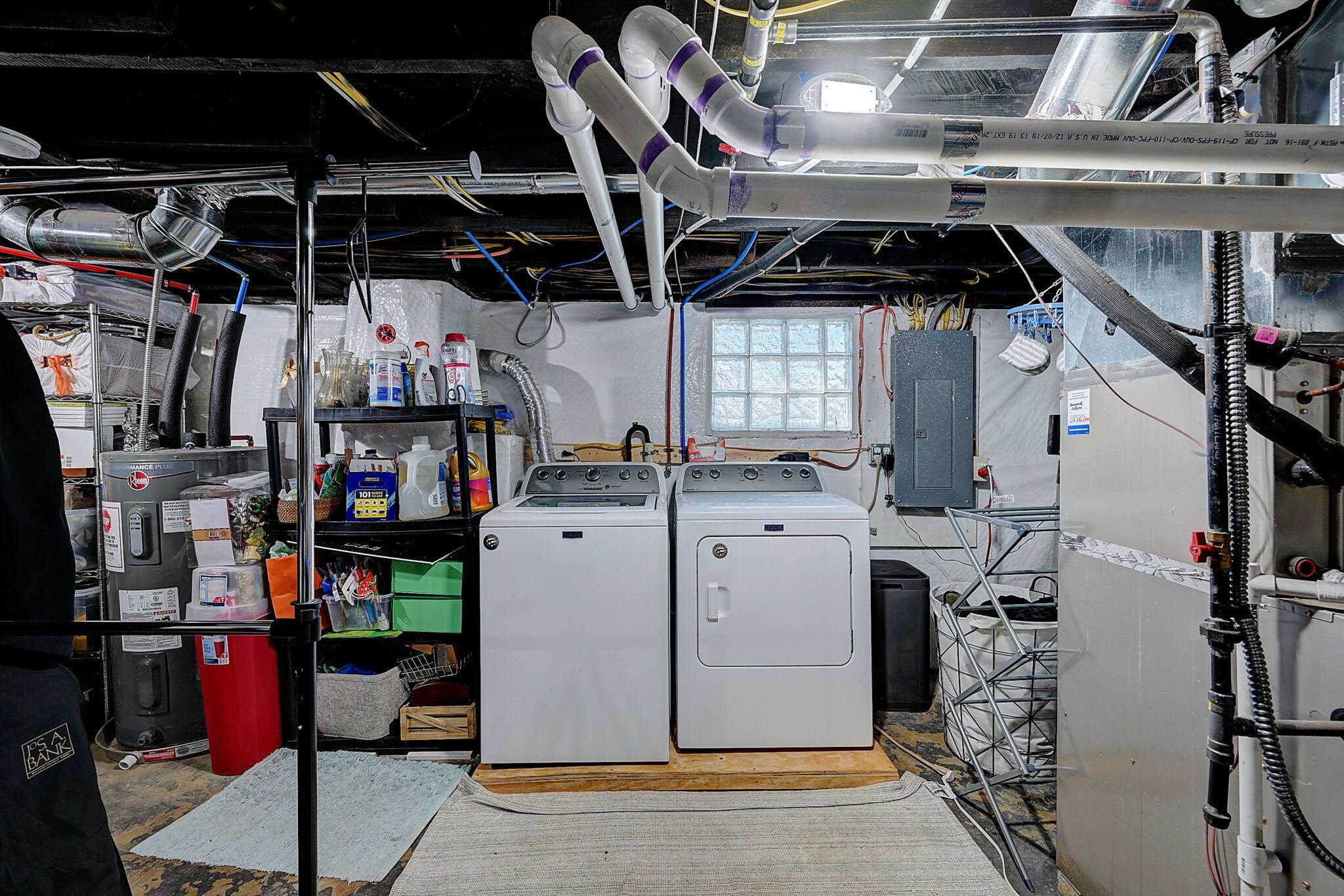Basement laundry area with a washer and dryer beneath exposed pipes and ductwork.