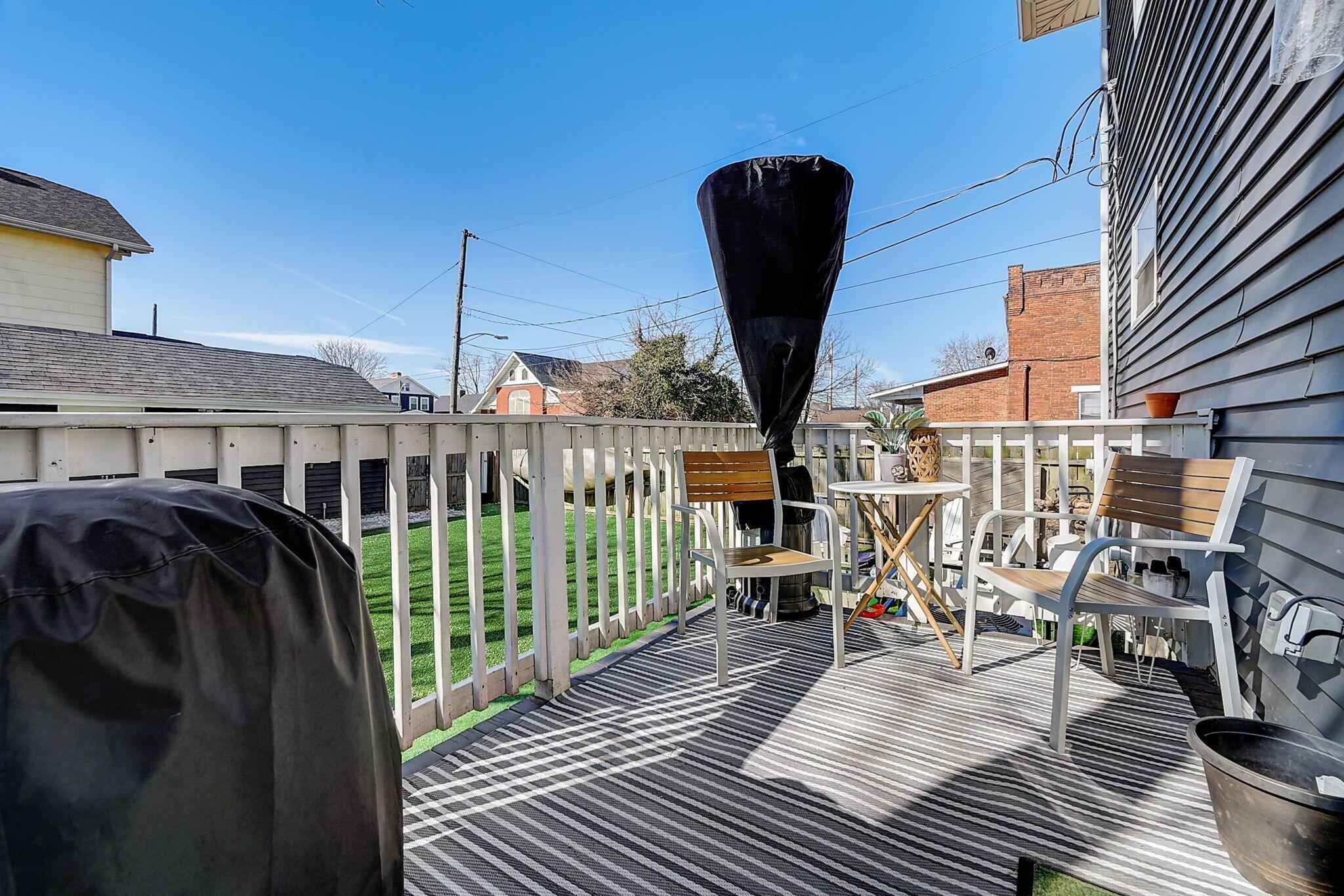Furnished backyard deck with a striped rug, seating, and covered grill.