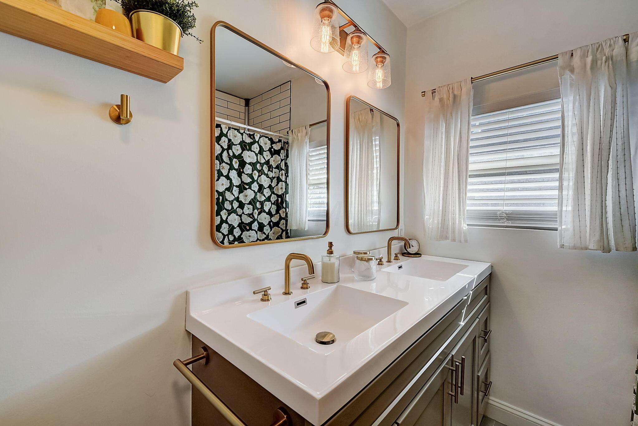 Bathroom with a double-sink vanity, brass fixtures, and mirrors reflecting a floral shower curtain.
