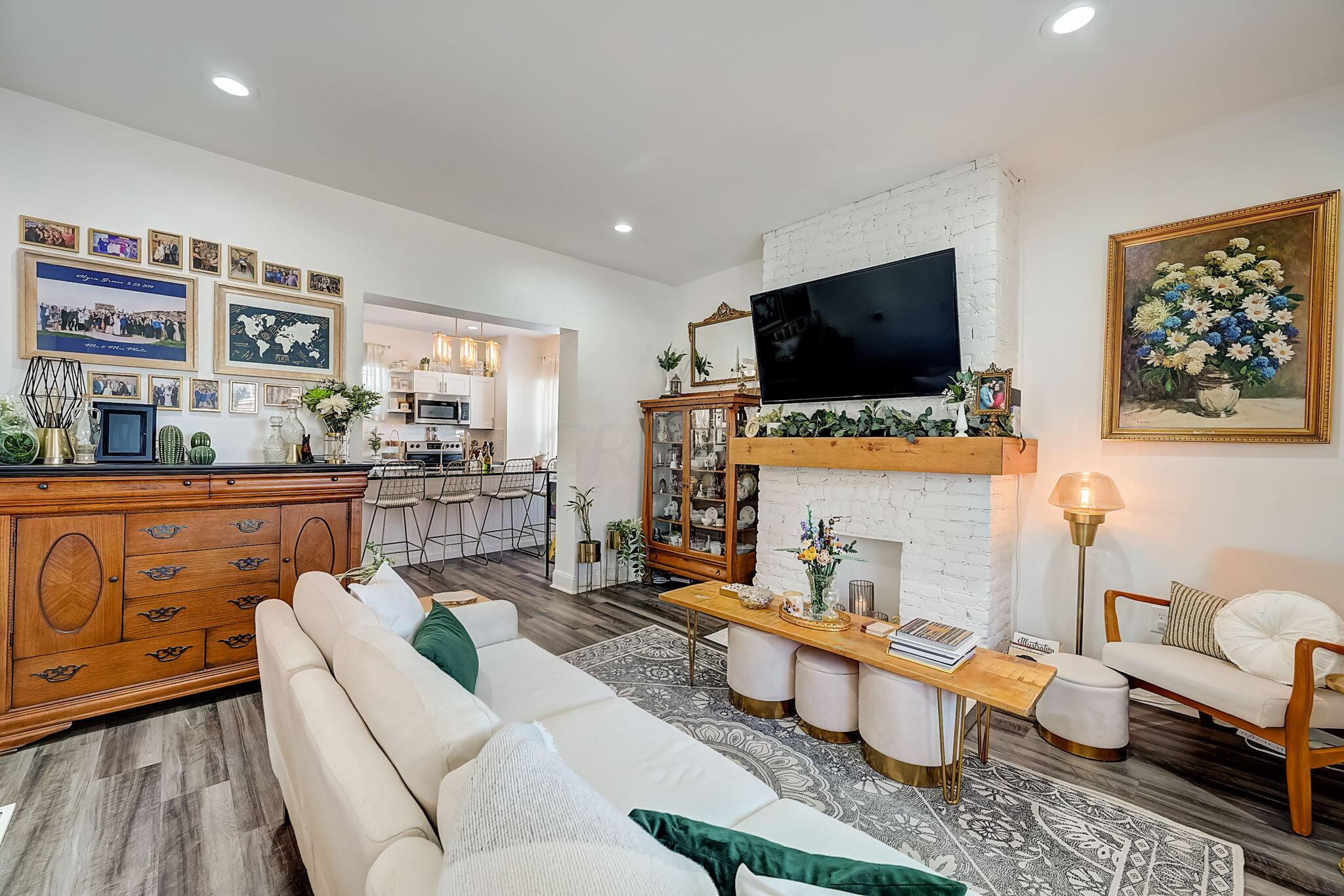 Living room with a white brick fireplace, large television, and open kitchen beyond.