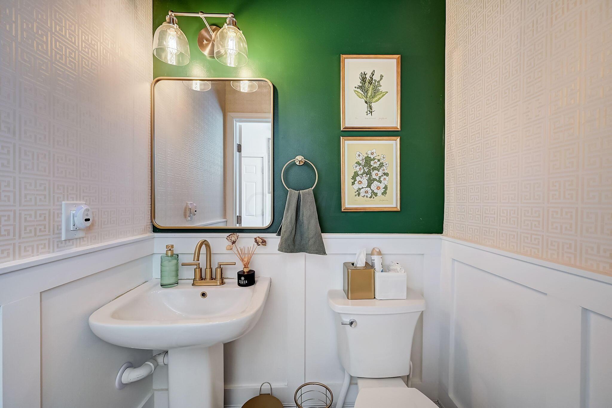 Bathroom with a pedestal sink, brass fixtures, and a dark green accent wall.