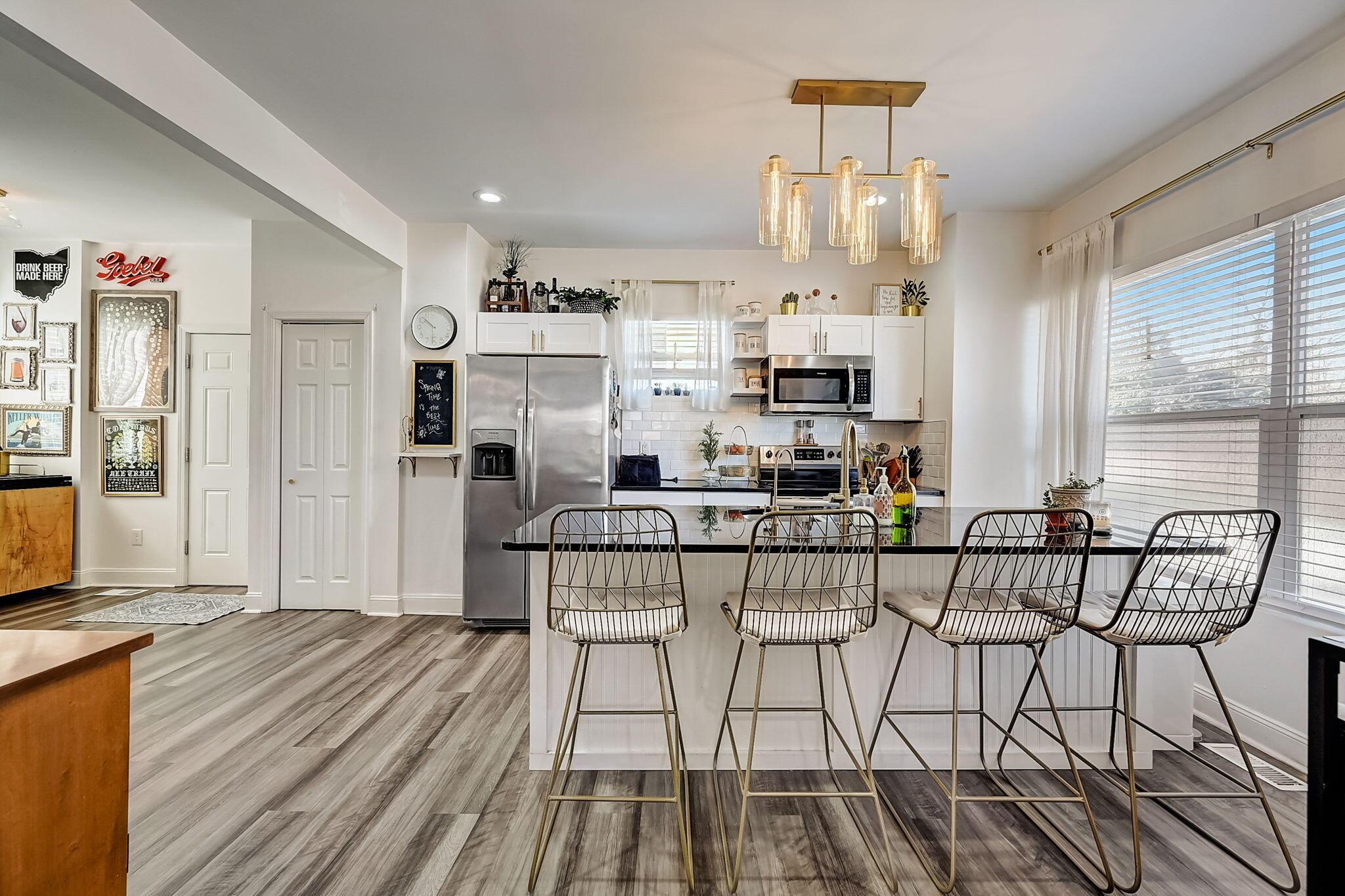 Open kitchen with stainless steel appliances, a black island, and four wire-frame bar stools.