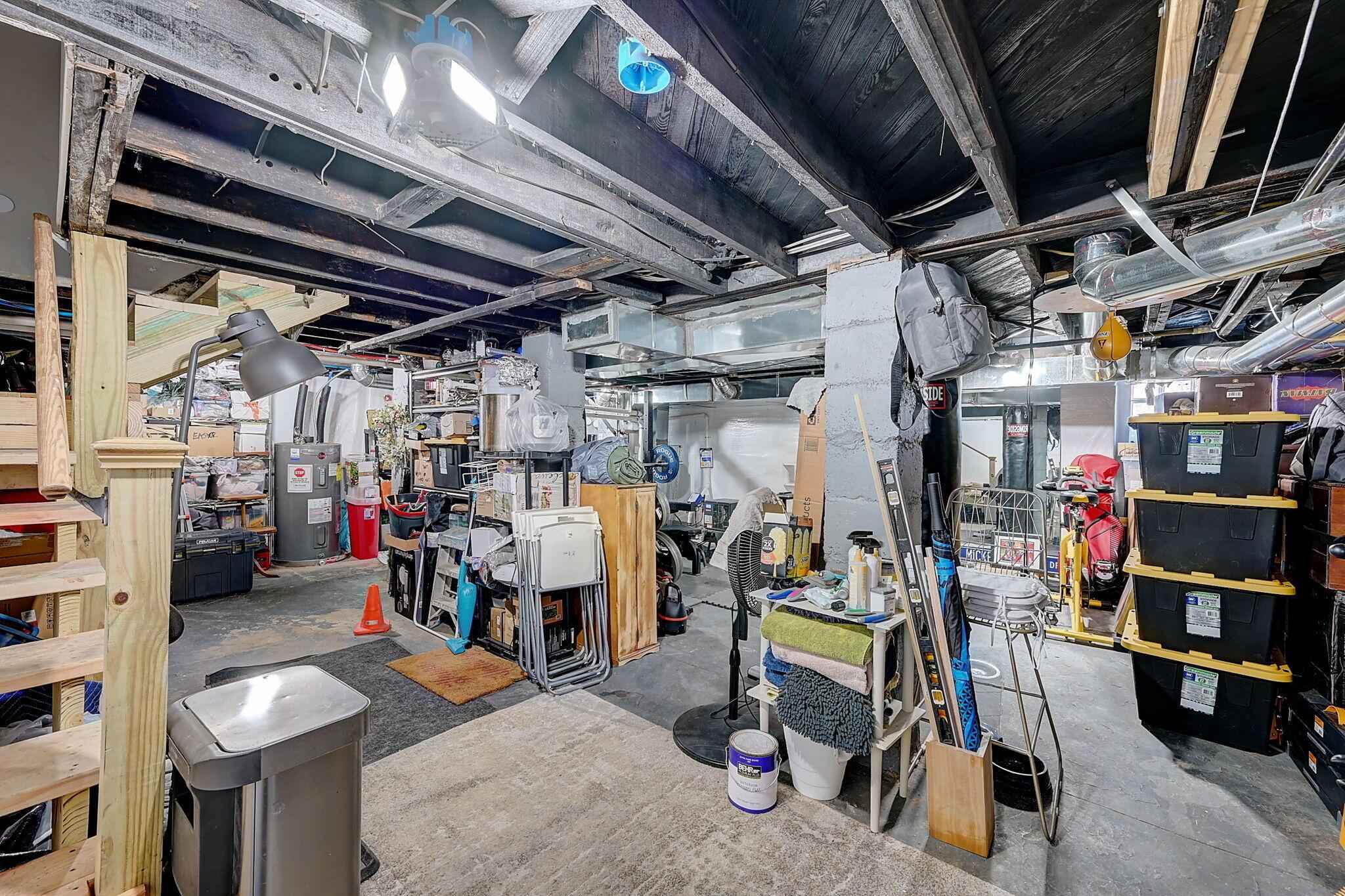 Unfinished basement crowded with storage bins, tools, folding chairs, and exposed ceiling joists.