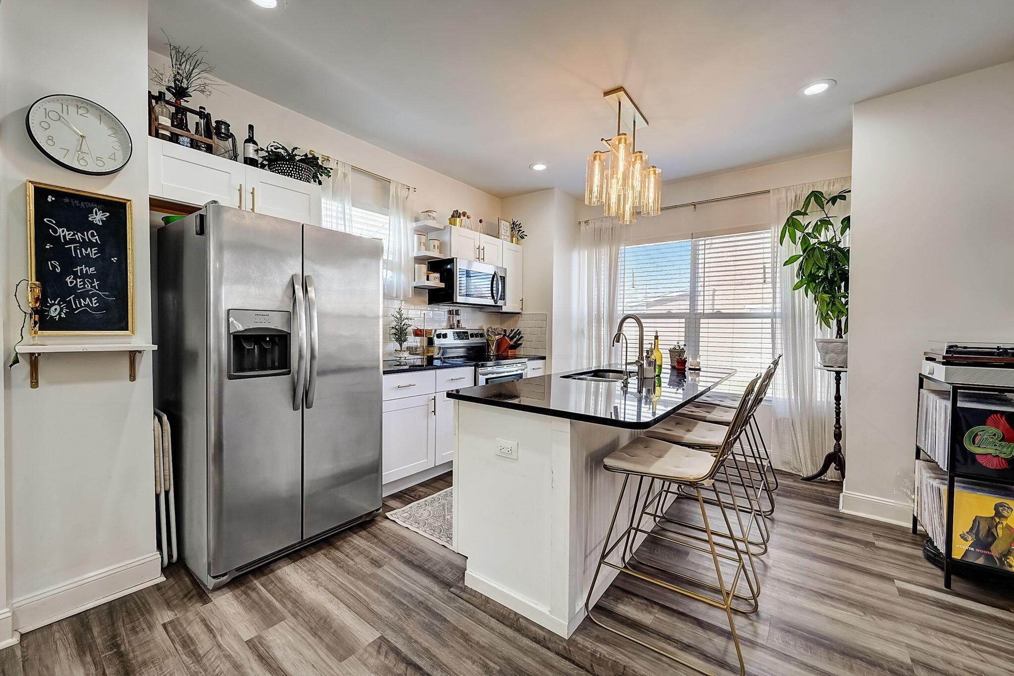 Bright kitchen with stainless steel appliances, a black island, bar stools, and a cluster of glass pendant lights.