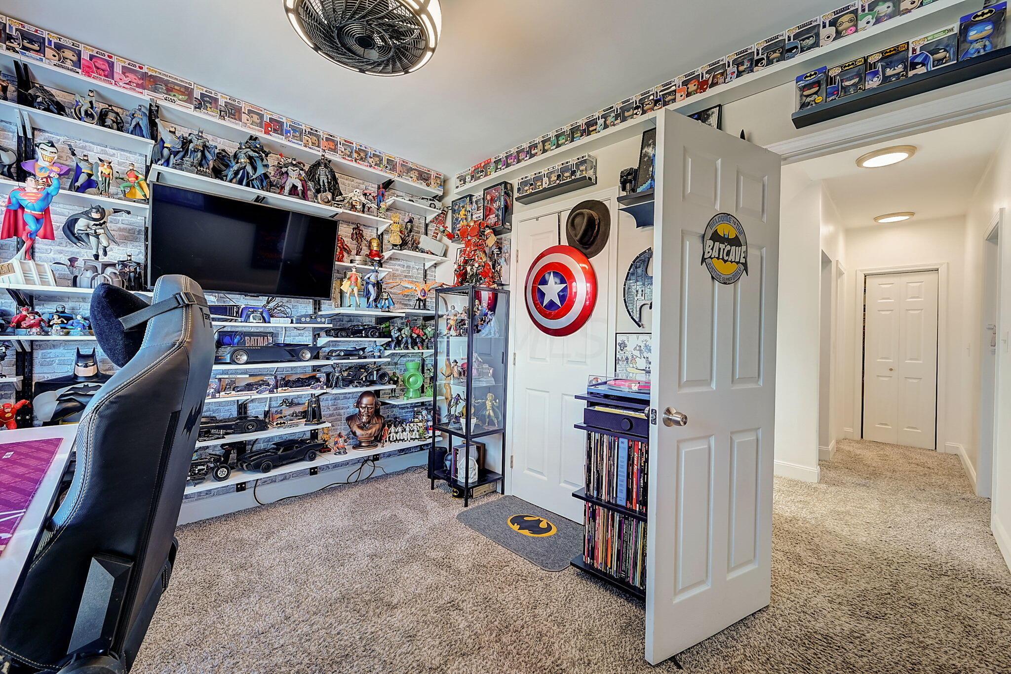 Collector’s room with superhero displays, model cars, a television, and a BATCAVE sign.