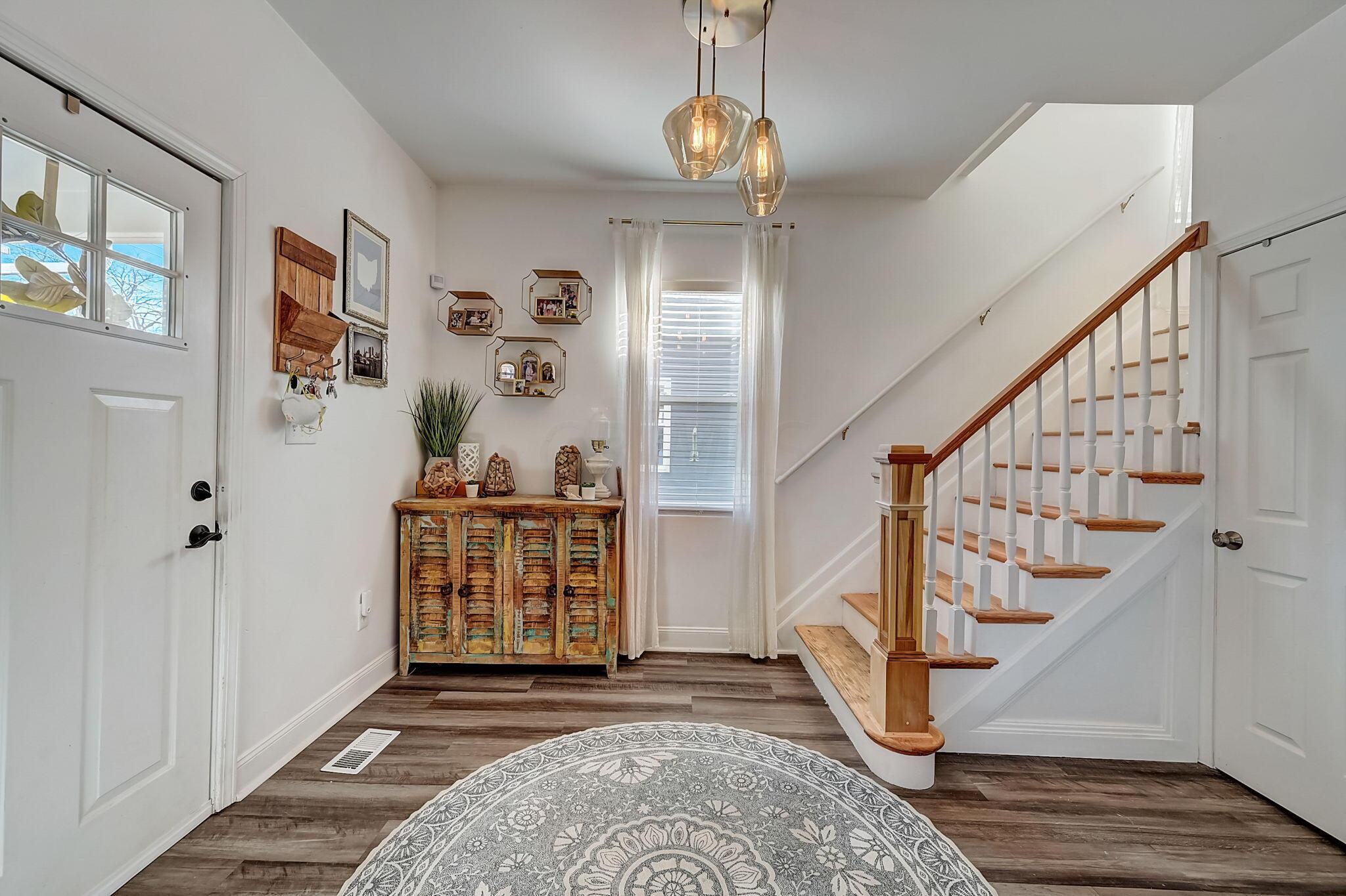 Entryway with a wood-and-white staircase, rustic console cabinet, and glass pendant lights.