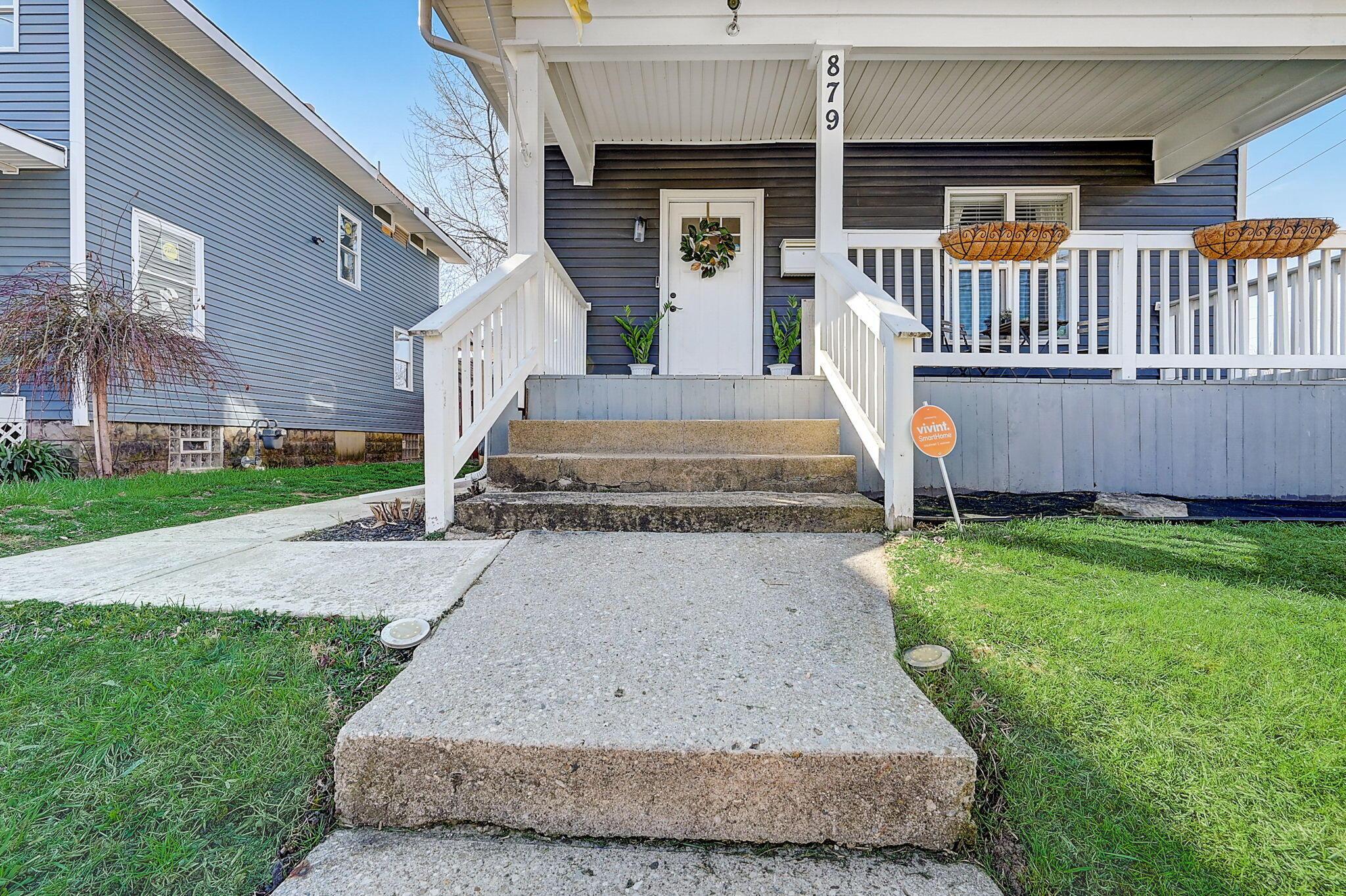 Home entrance with dark blue siding, white covered porch, concrete steps, and hanging planters.