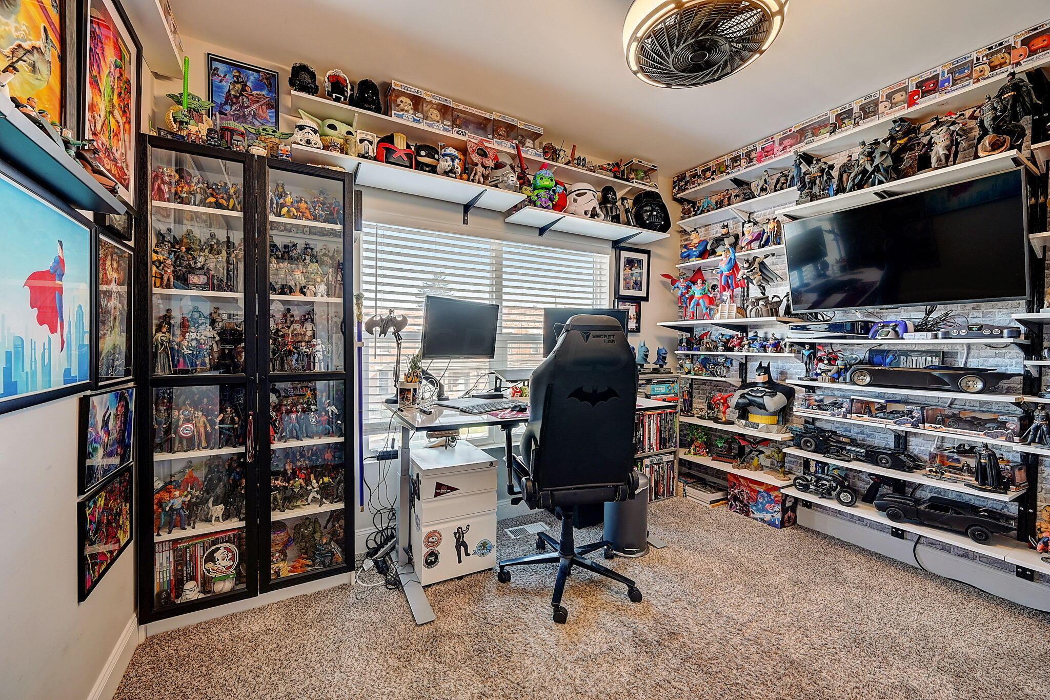 Home office lined with superhero collectibles, featuring a desk, gaming chair, and large television.