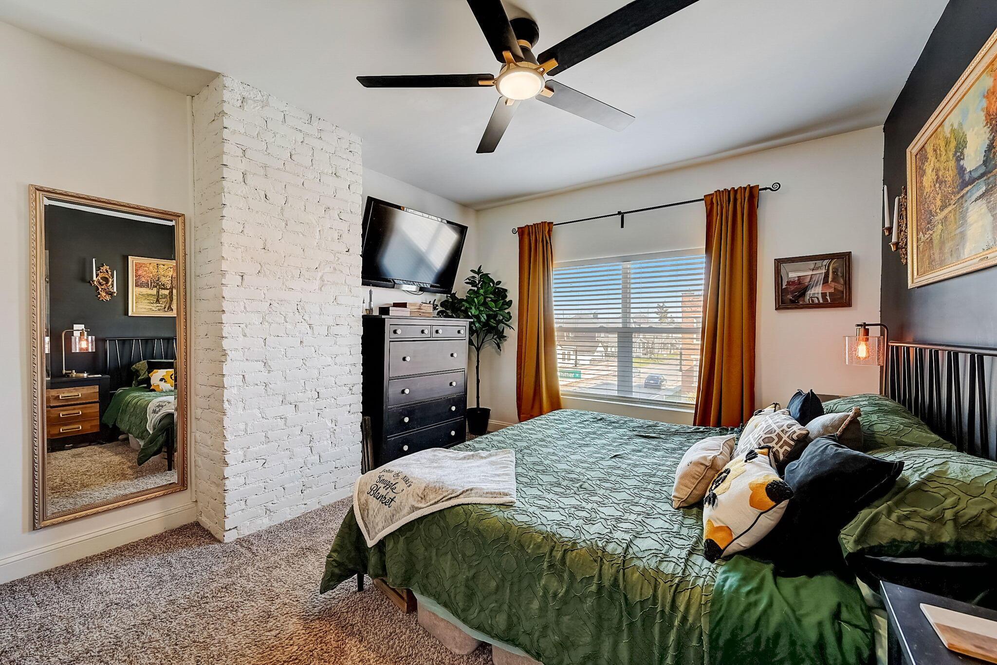 Bedroom with a green quilted bed, white brick column, and rust-colored curtains framing the window.