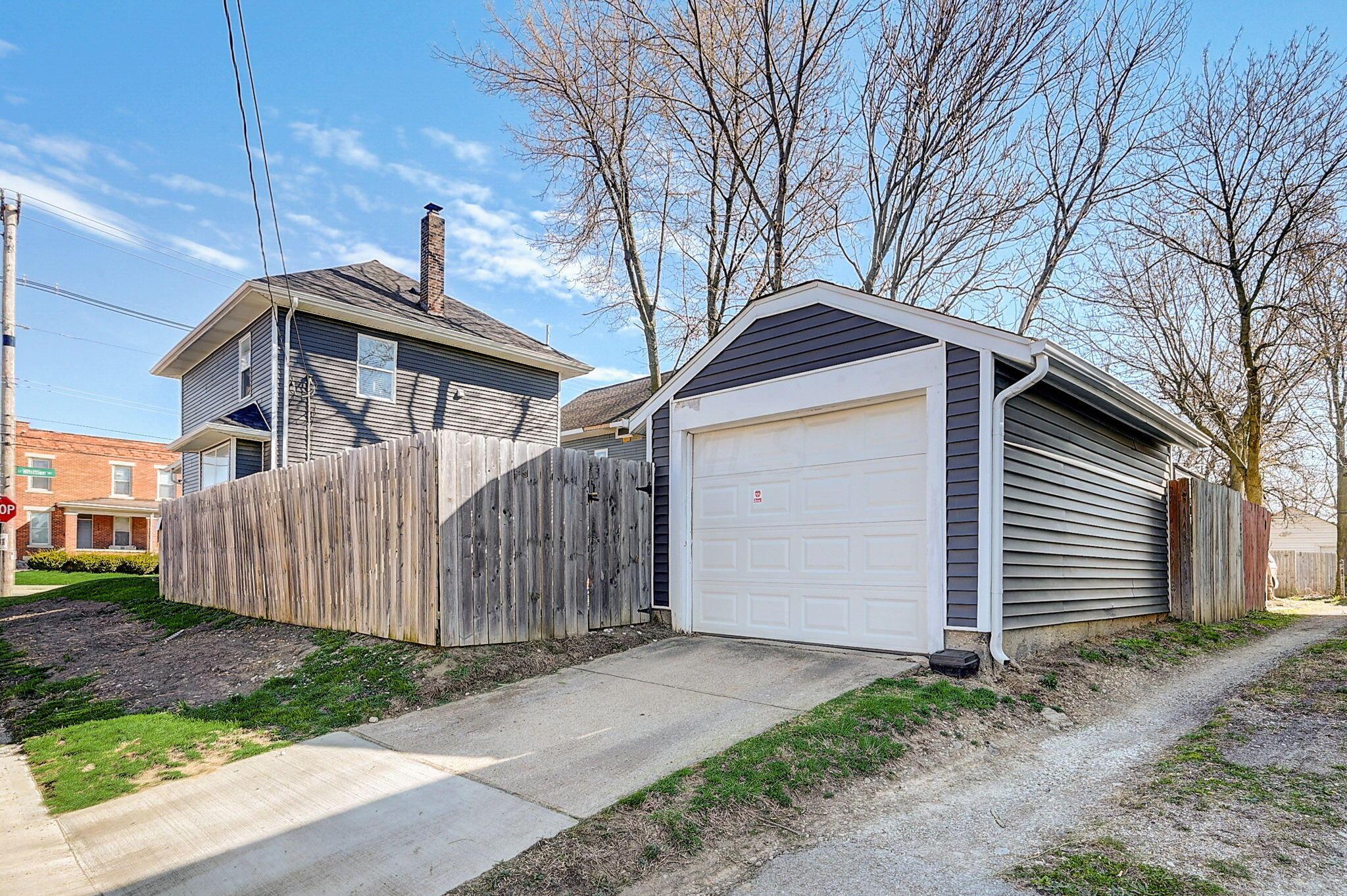 Detached gray garage with a white door, wooden privacy fence, and concrete driveway.